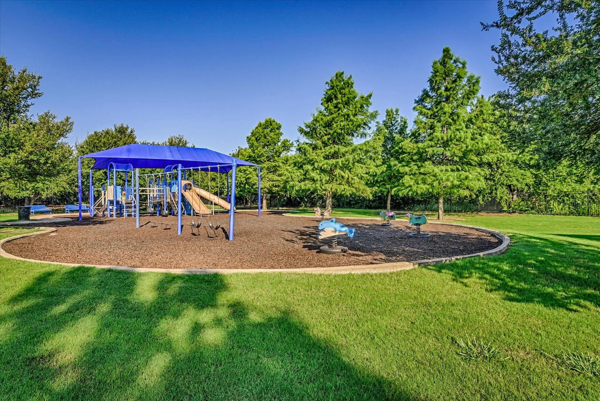 Community playground featuring a blue shade canopy, integrated slide, swing set, and spring riders