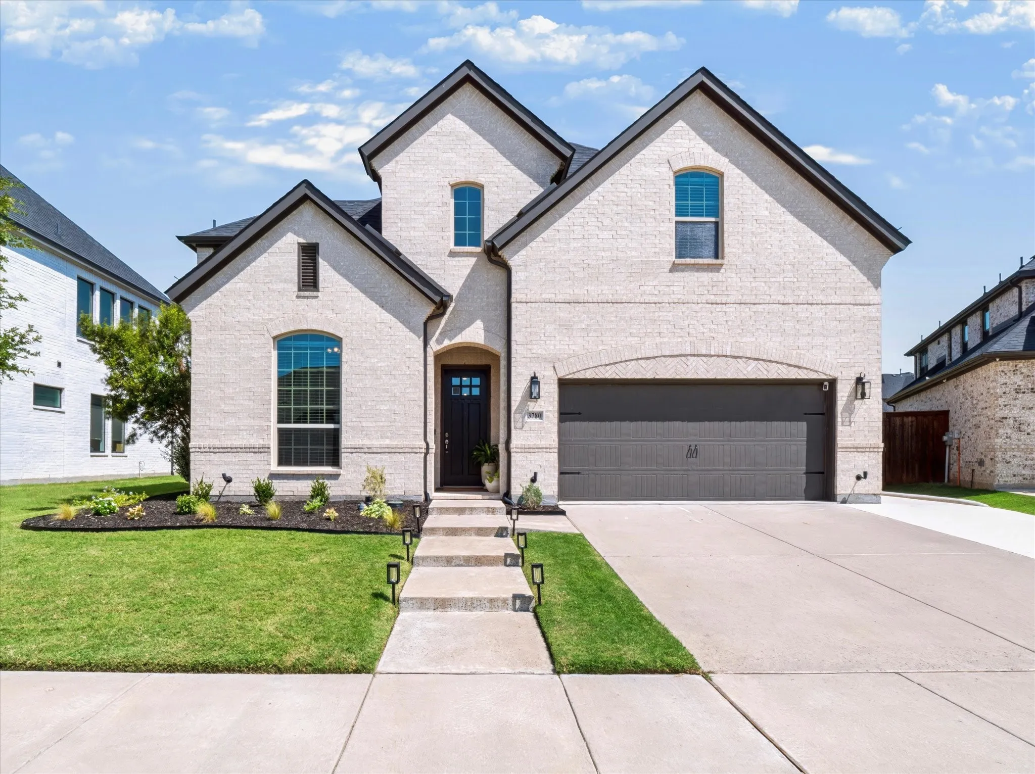 Light brick exterior, dark trim accents, arched garage door, extended concrete driveway, and front landscaping