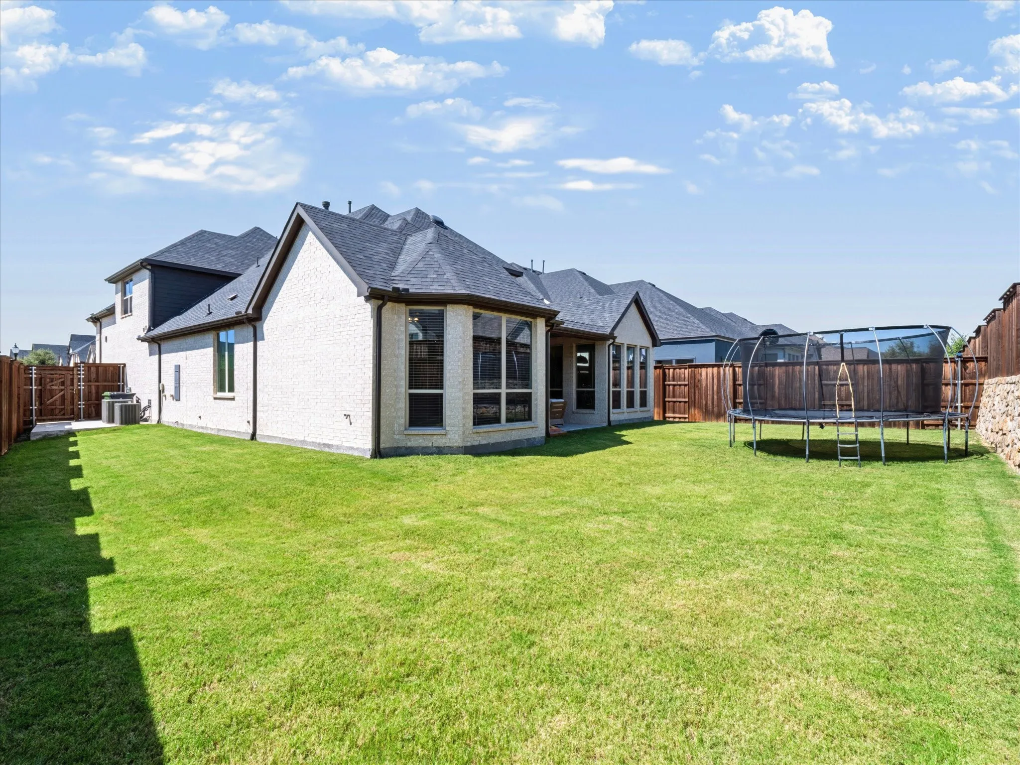 Expansive backyard featuring a manicured lawn, full privacy fencing, and a stucco exterior with multiple windows