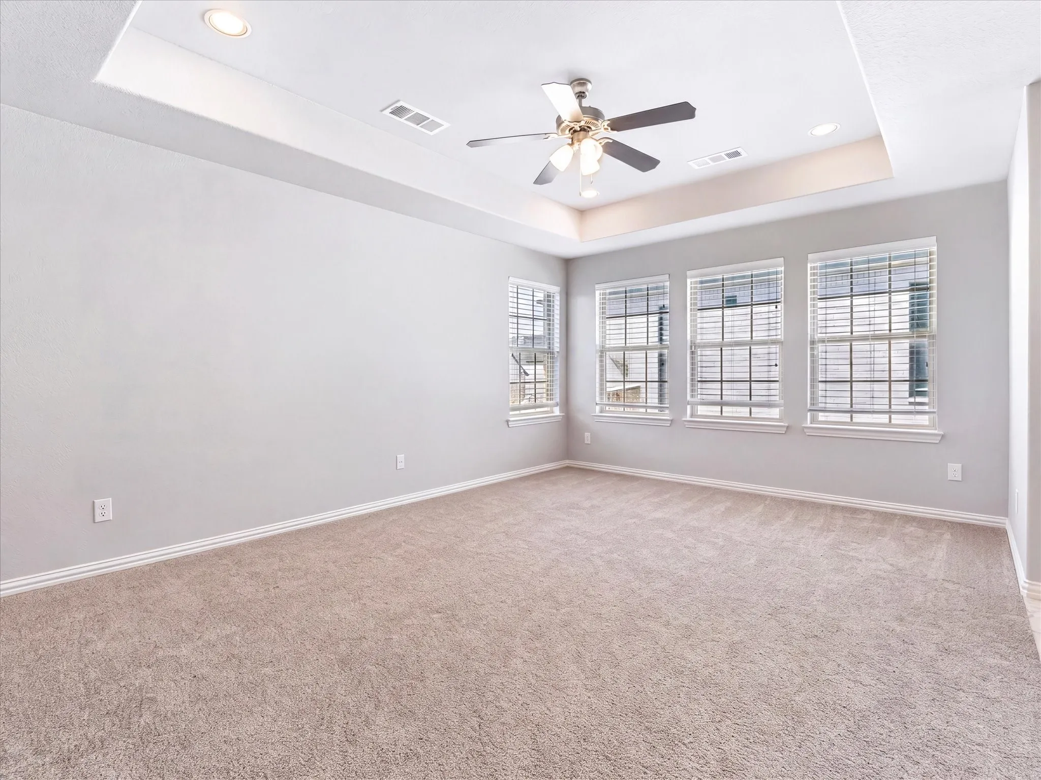 Bright, open room featuring neutral wall finishes, plush carpeting, and abundant natural light from four large windows with grid-pattern panes