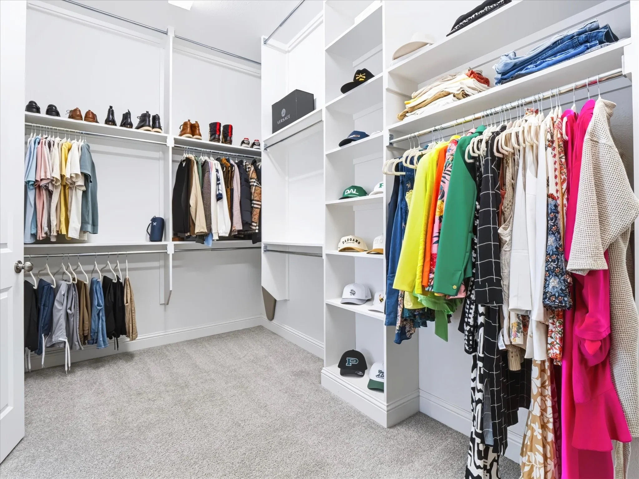 Custom-built closet system featuring extensive shelving, multiple hanging rods, white cabinetry, and light gray carpeting