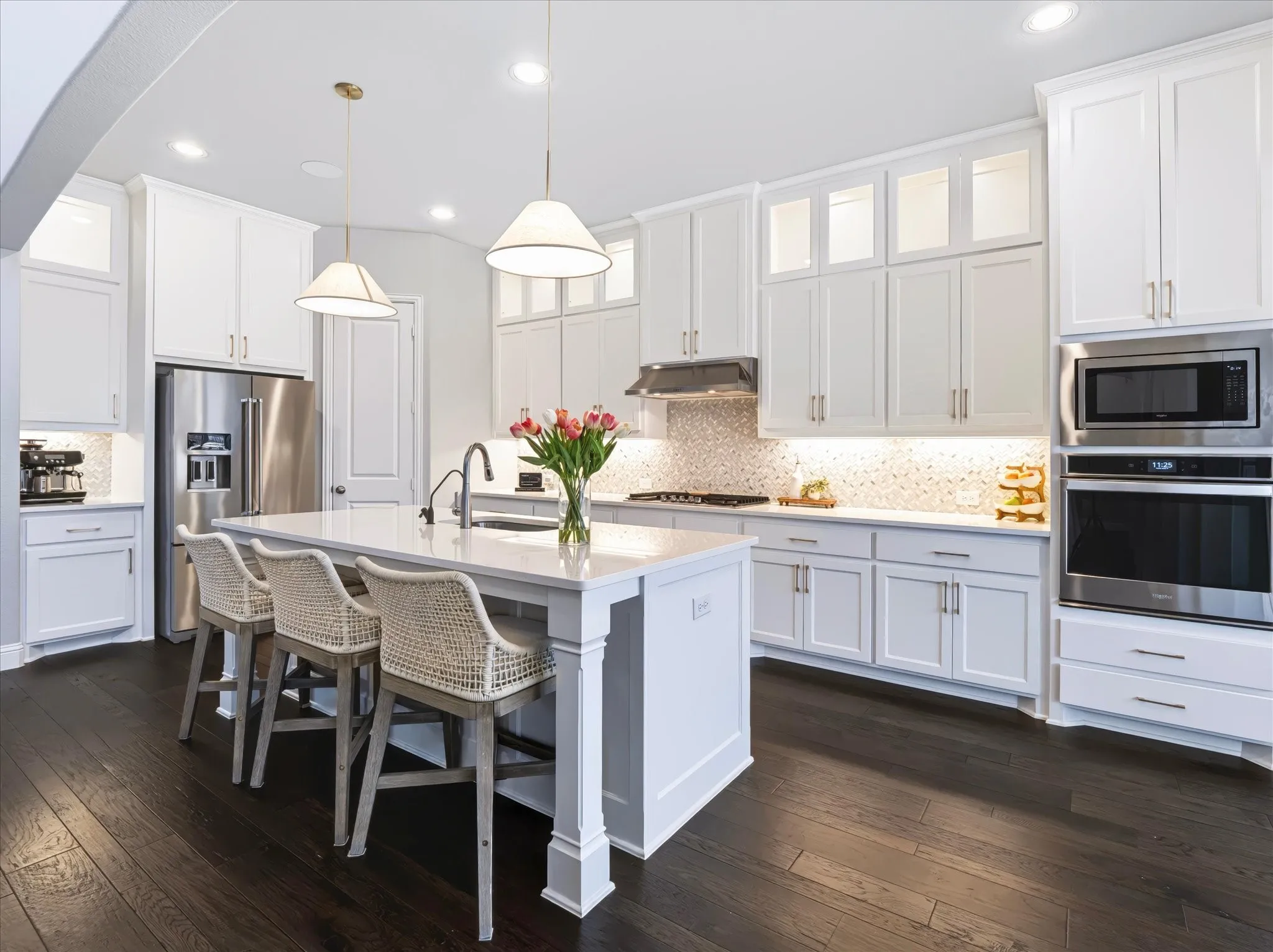 Spacious kitchen featuring an expansive island, white cabinetry, integrated stainless steel appliances, a tile backsplash, and dark wood-finish flooring