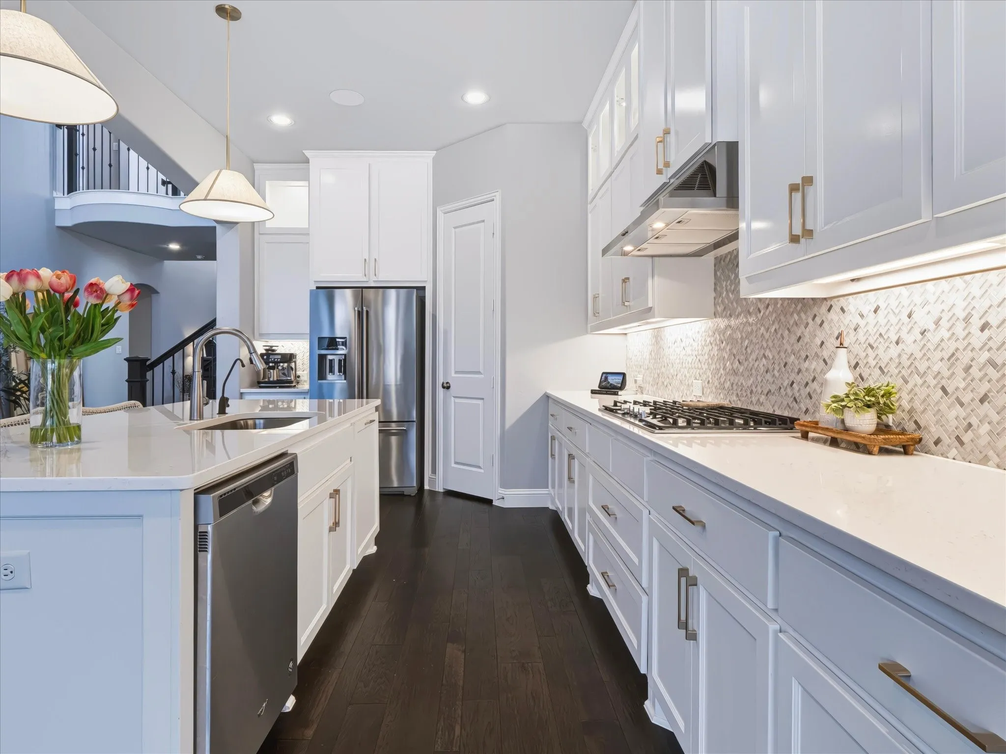 Kitchen featuring dark wood-finish flooring, white cabinetry with gold-toned hardware, stainless steel appliances, and a tiled backsplash