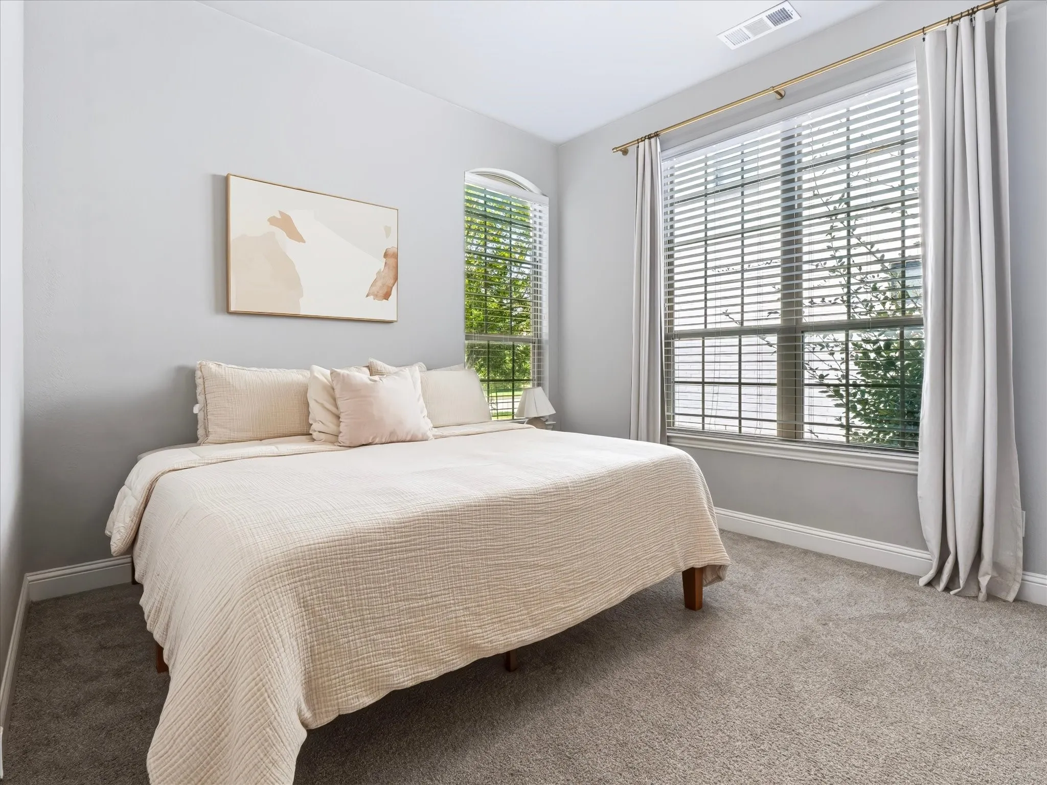 Light gray wall paint, large window with blinds, gold curtain rods, gray carpeting, and a second arched window
