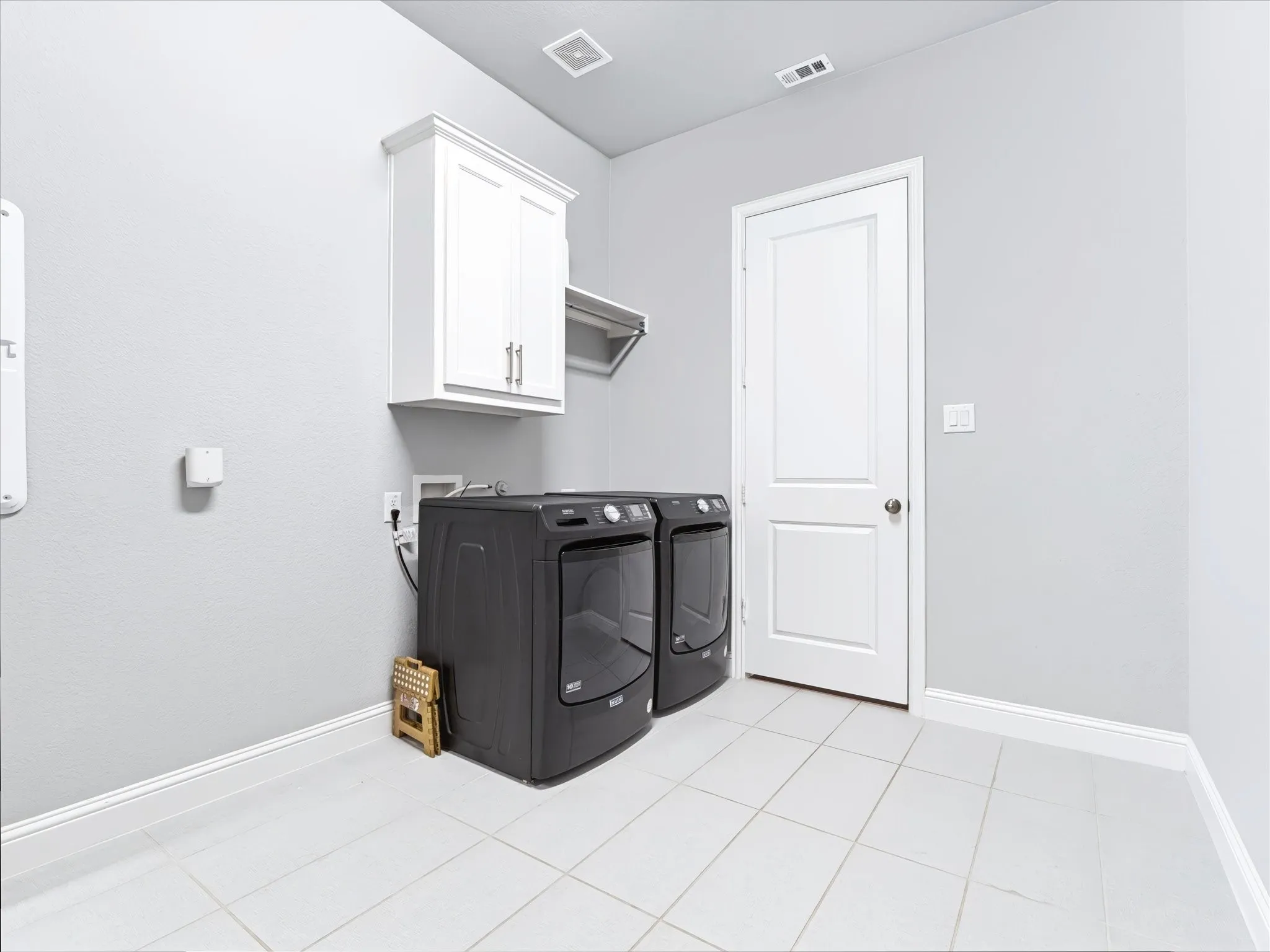 Laundry area featuring light-toned tile flooring, white shaker-style cabinetry, and a wall-mounted shelving unit