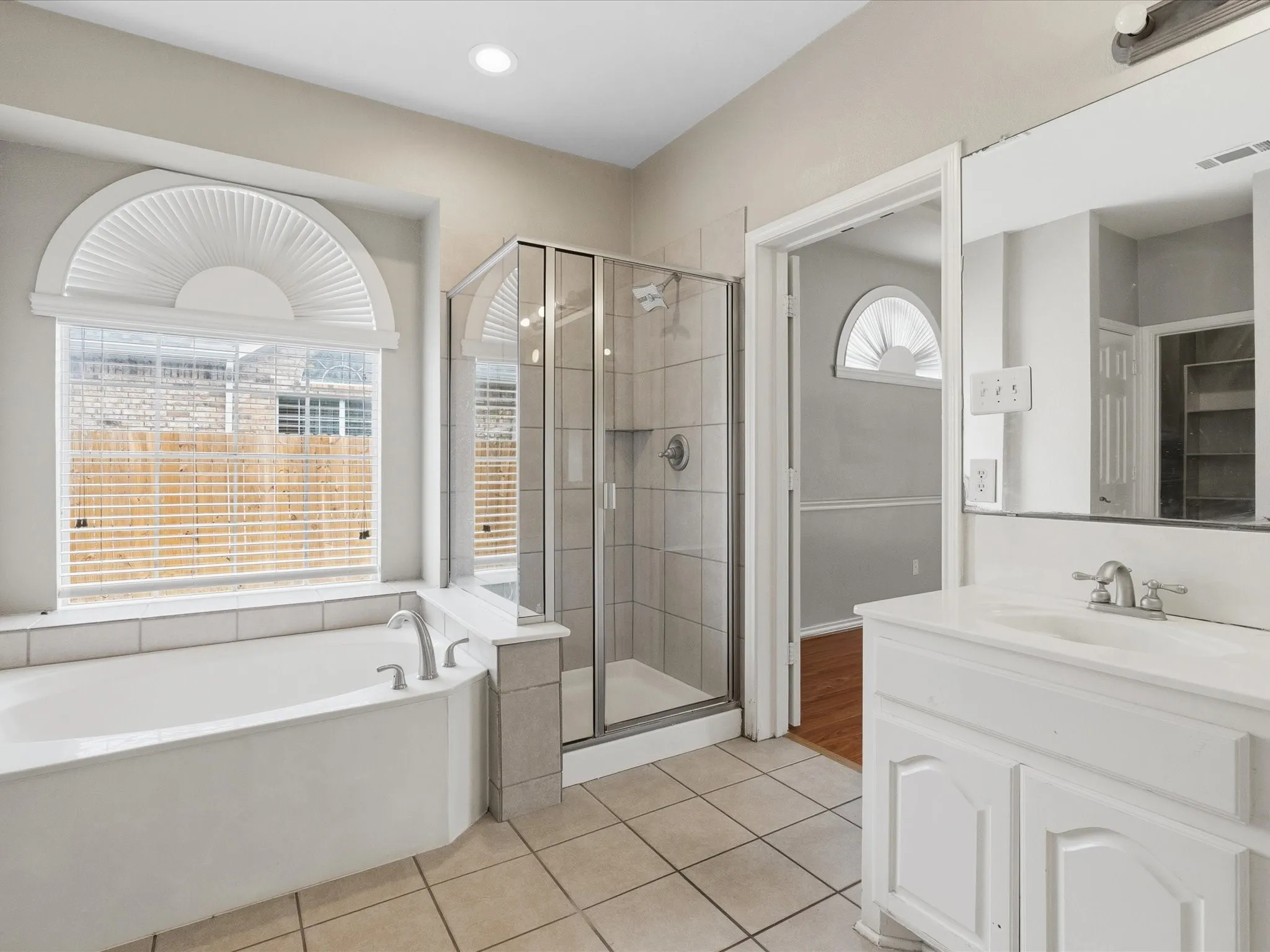 Full bathroom featuring a white soaking tub with silver fixtures, a glass-enclosed shower, a white vanity with an integrated sink, and large format tile flooring