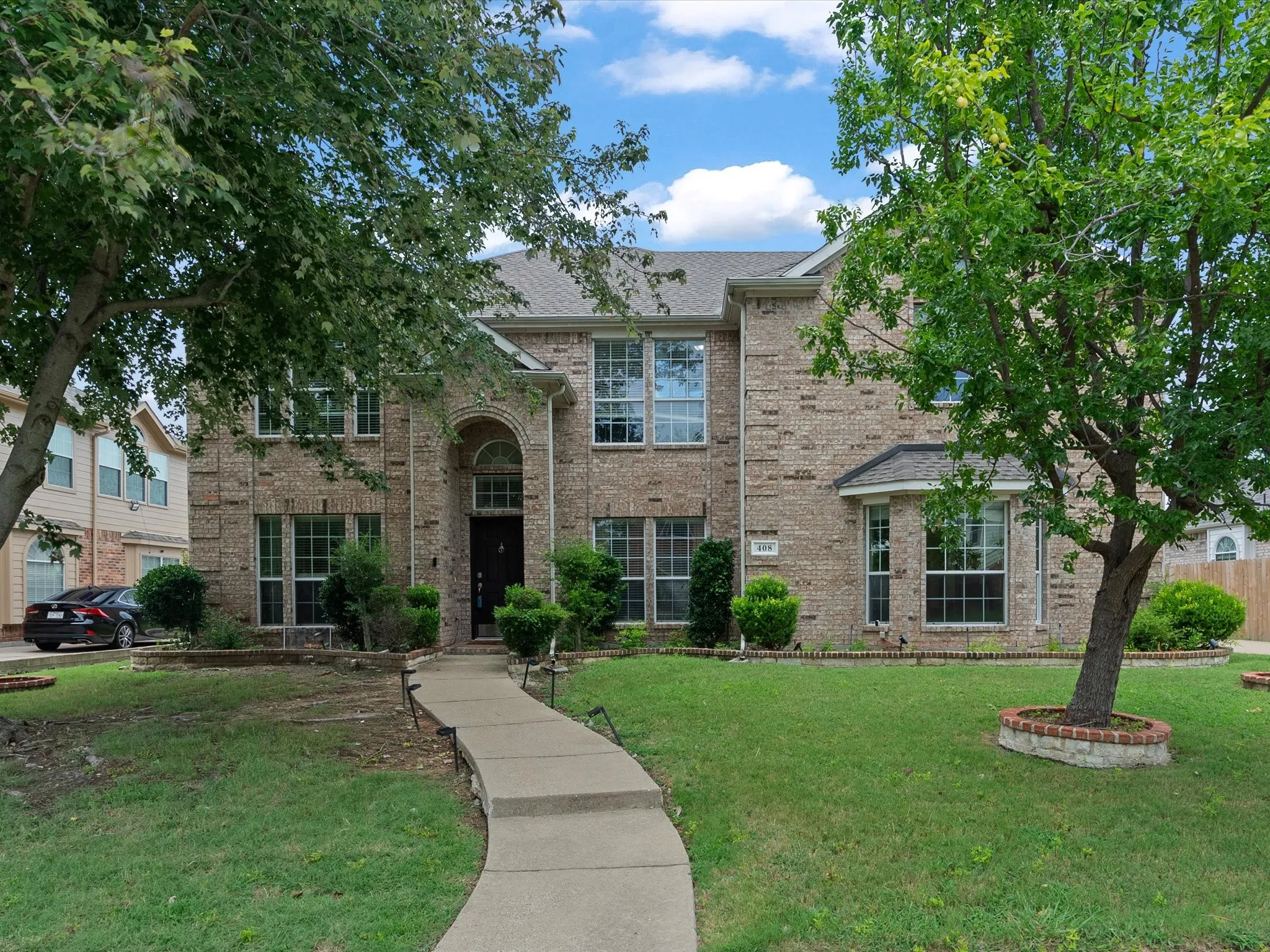 Two-story brick exterior featuring a prominent arched entryway, multiple large windows, and a concrete pathway