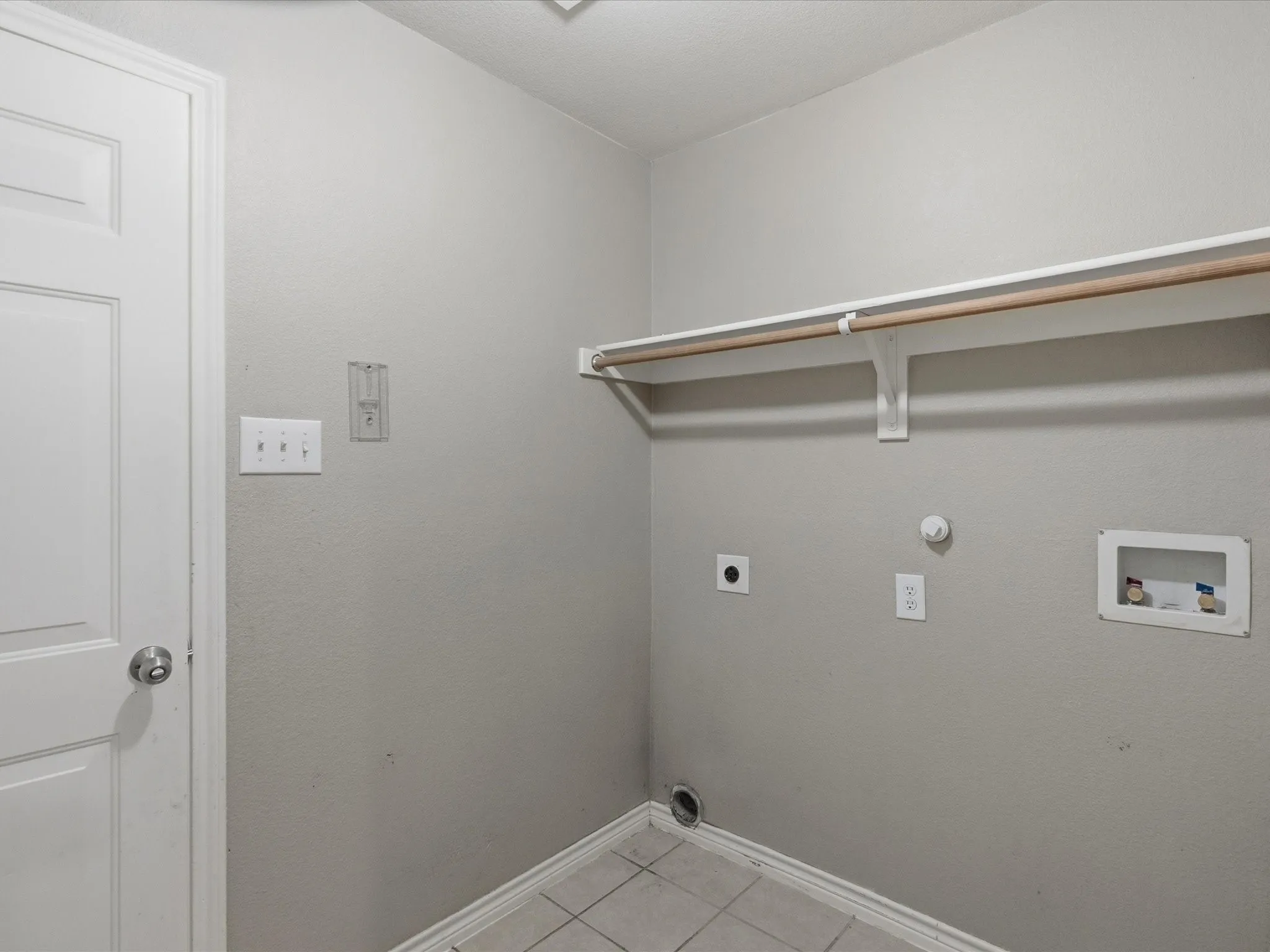 Dedicated utility space featuring tile flooring, neutral wall tones, a white paneled door, and a built-in hanging rod with shelving