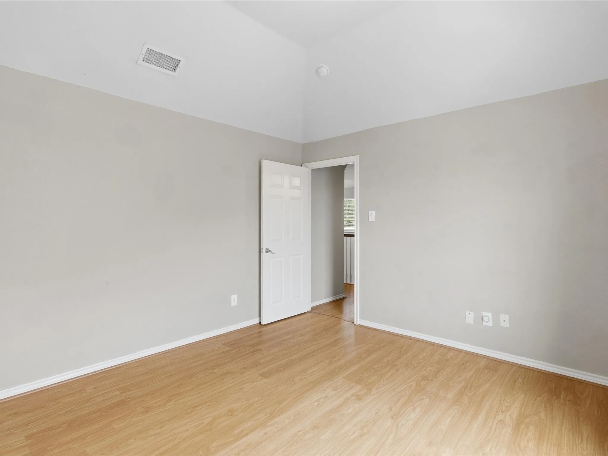 Vaulted ceiling with a recessed vent, wood-finish flooring, light gray wall paint, and white trim molding