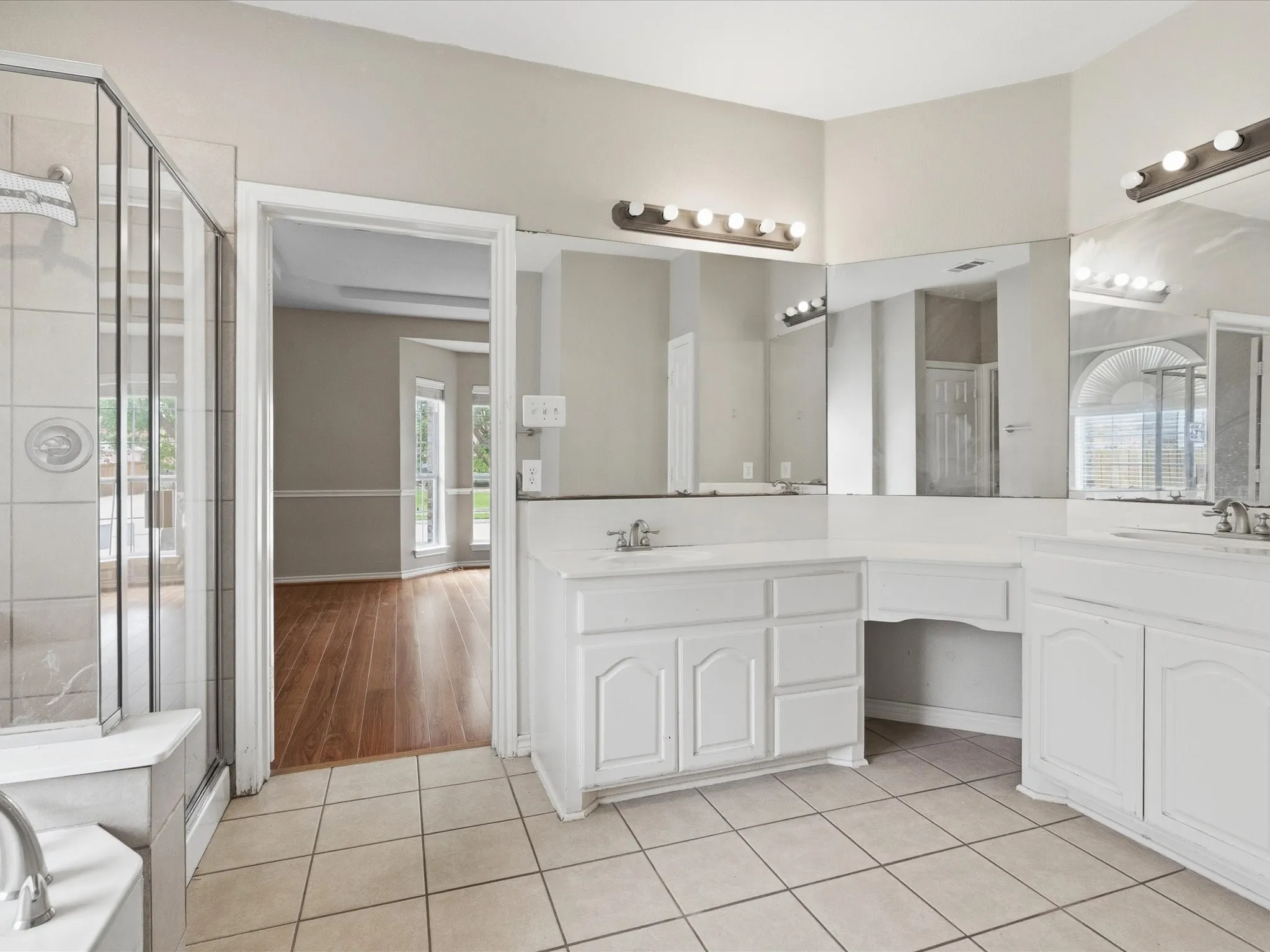 Bathroom featuring dual white vanity cabinets, extensive mirror coverage, tiled flooring, an enclosed shower, and a separate bathtub