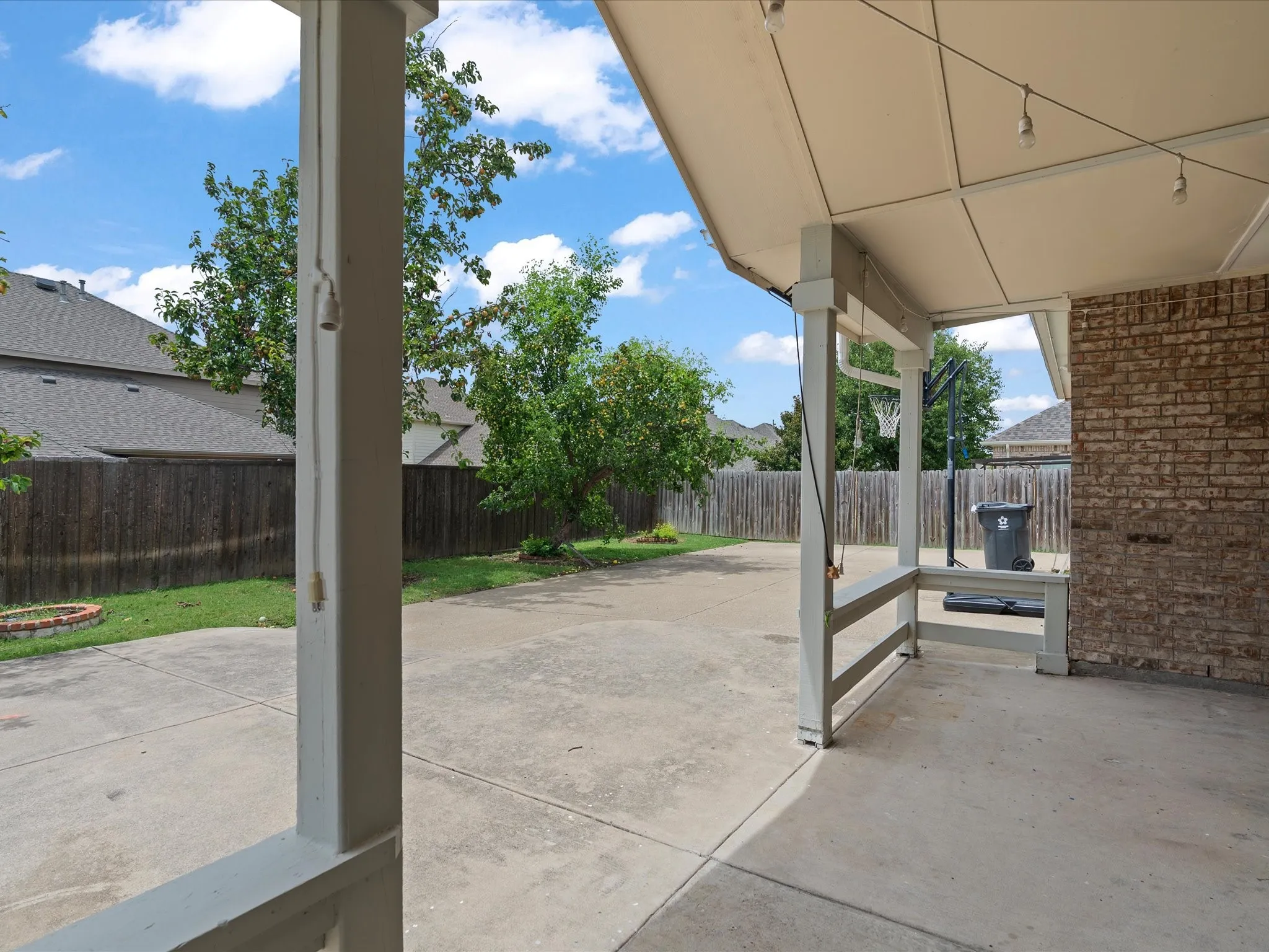 Covered patio with brick exterior wall, concrete flooring, and string lighting