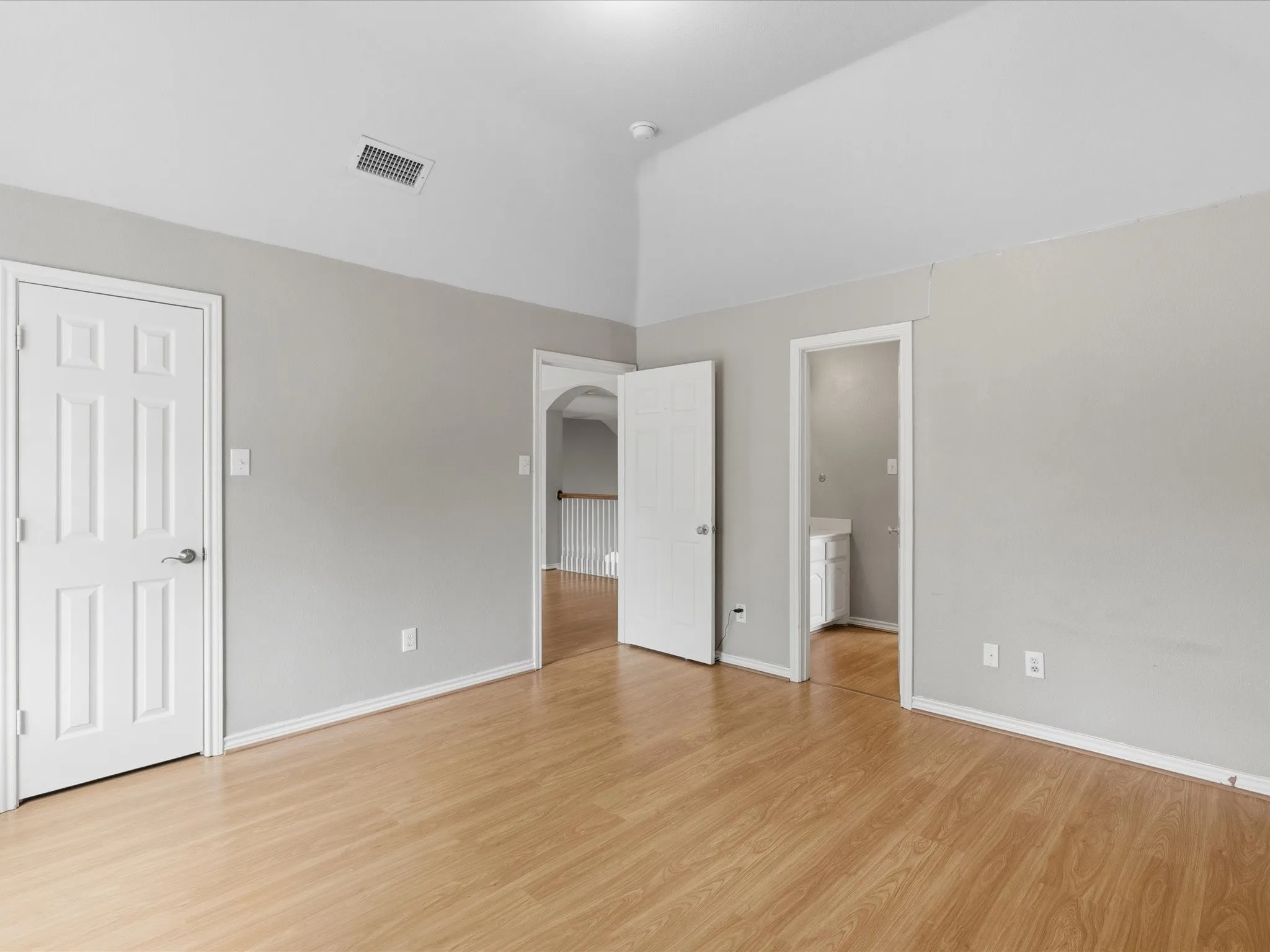 Vaulted ceiling room featuring light-toned wood-finish flooring, neutral gray walls, and white trim