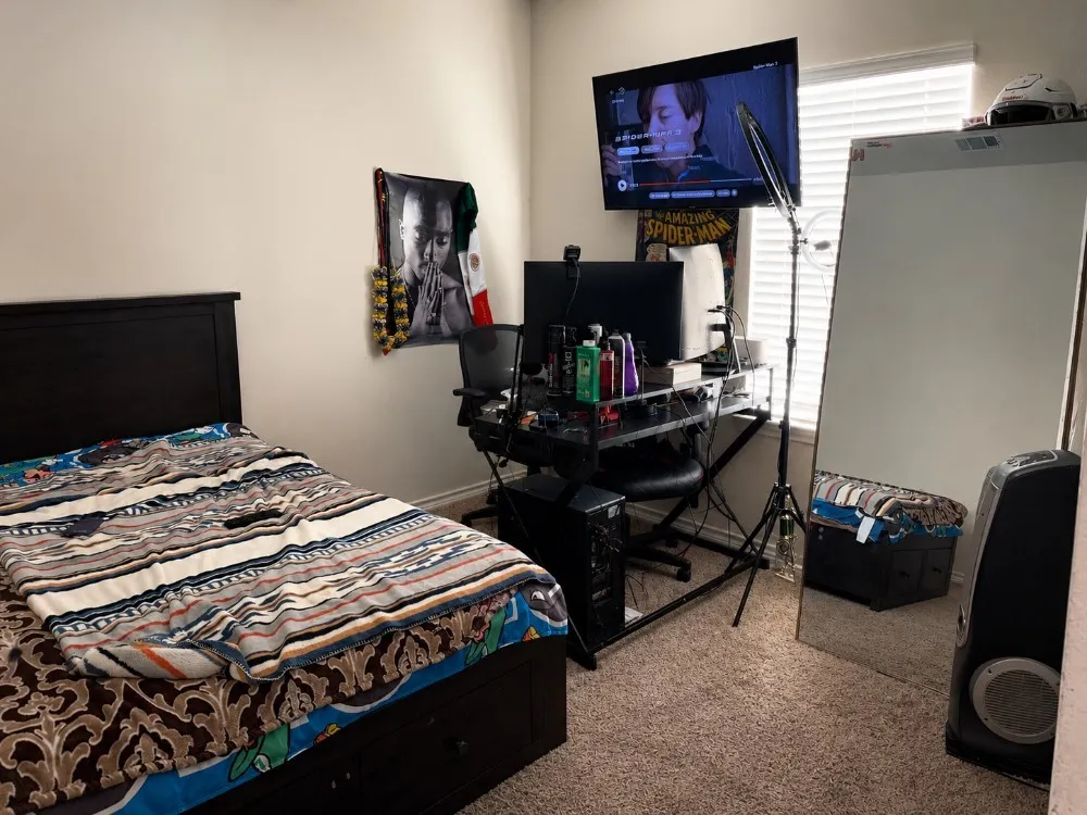 Bedroom featuring a dark wood headboard, light beige wall paint, carpeted flooring, window with blinds, and a wall-mounted television