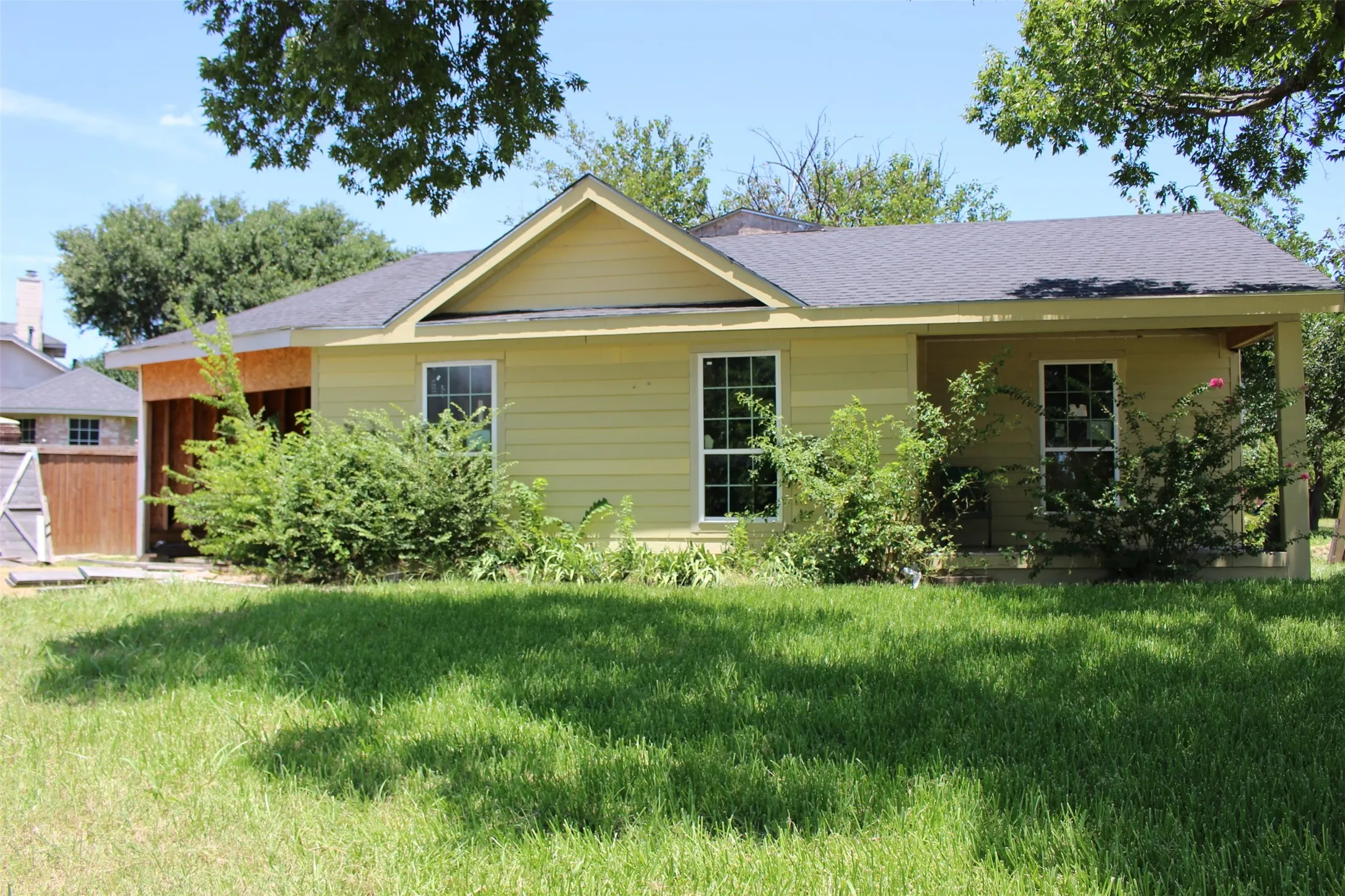 Single-story residence featuring light yellow siding and a dark shingle roof