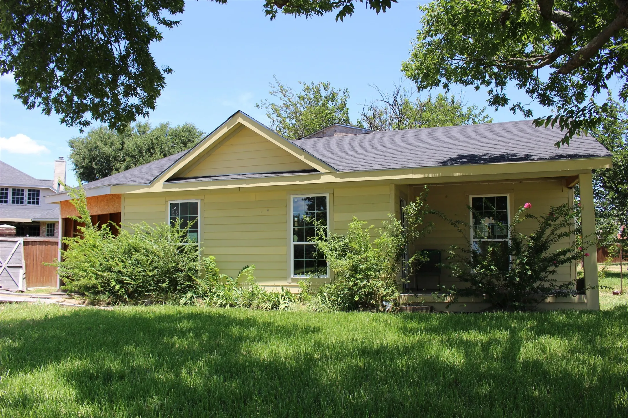 Single-story residence featuring light yellow siding and a dark shingle roof