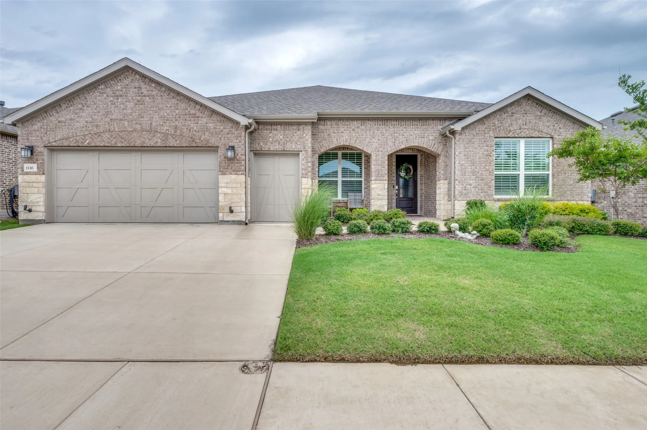 Brick exterior with stone accents, a three-car garage, and a well-maintained lawn