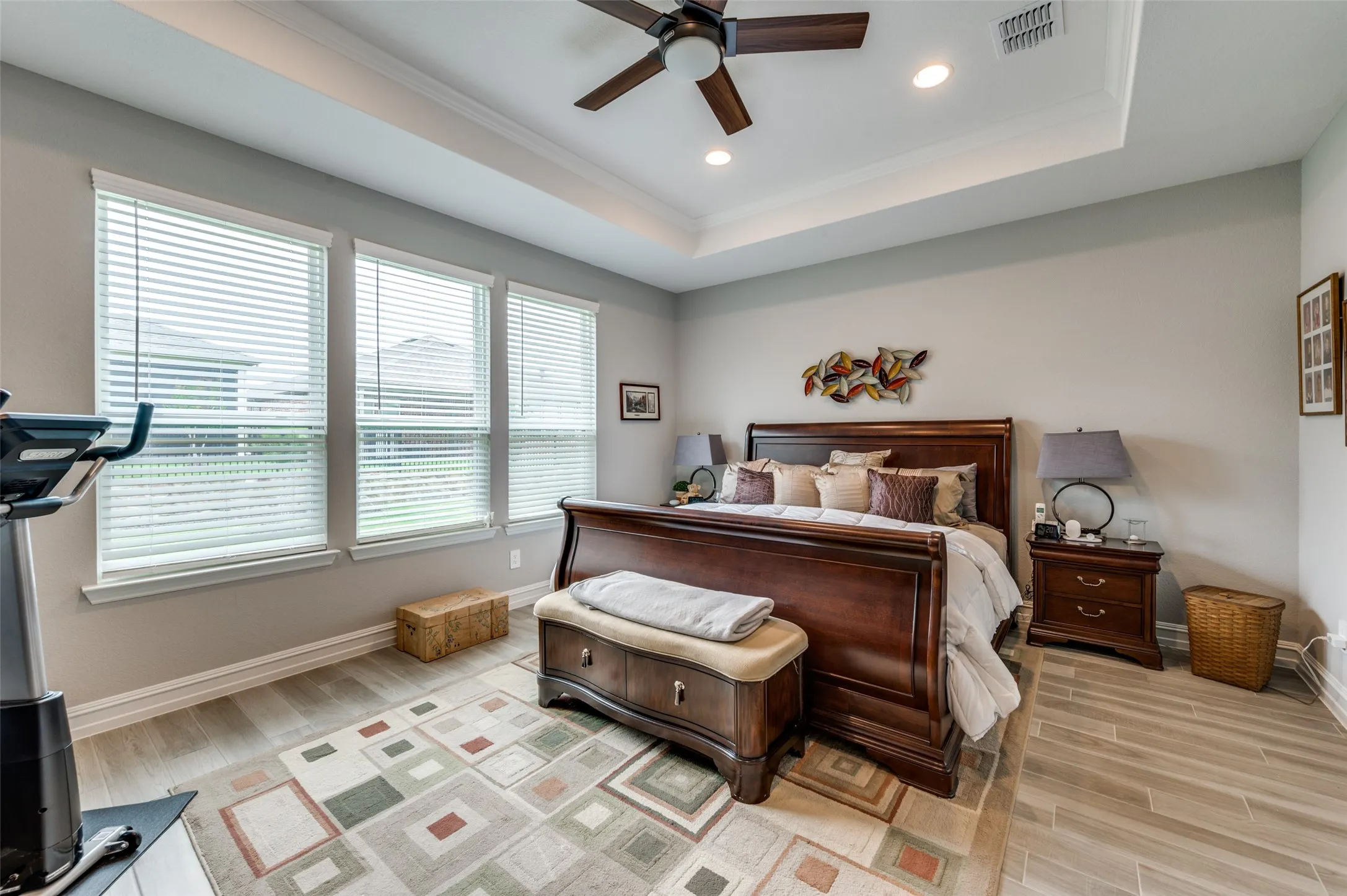 Spacious bedroom featuring a tray ceiling with a ceiling fan, recessed lighting, and wood-finish flooring