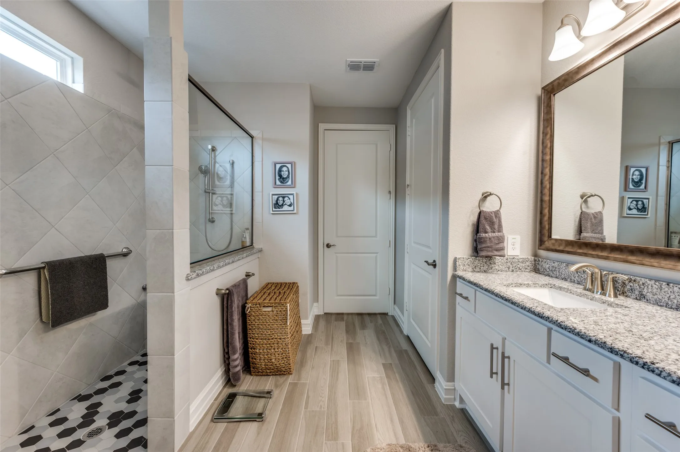 Spacious bathroom featuring a double vanity with stone countertops, a large framed mirror, a separate glass-enclosed shower with tile surround, and wood-finish flooring