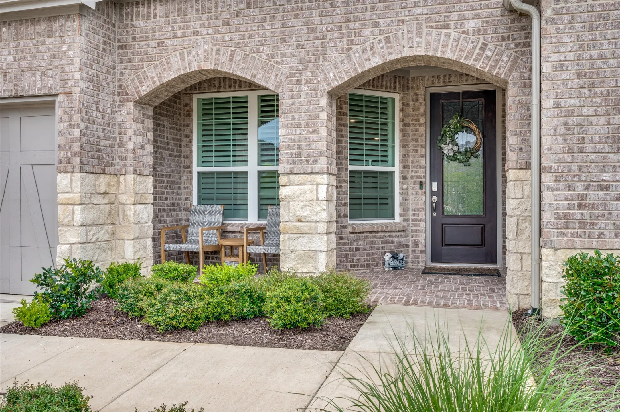 Brick and stone facade featuring an arched entry, dark panel door with decorative glass, and a covered porch