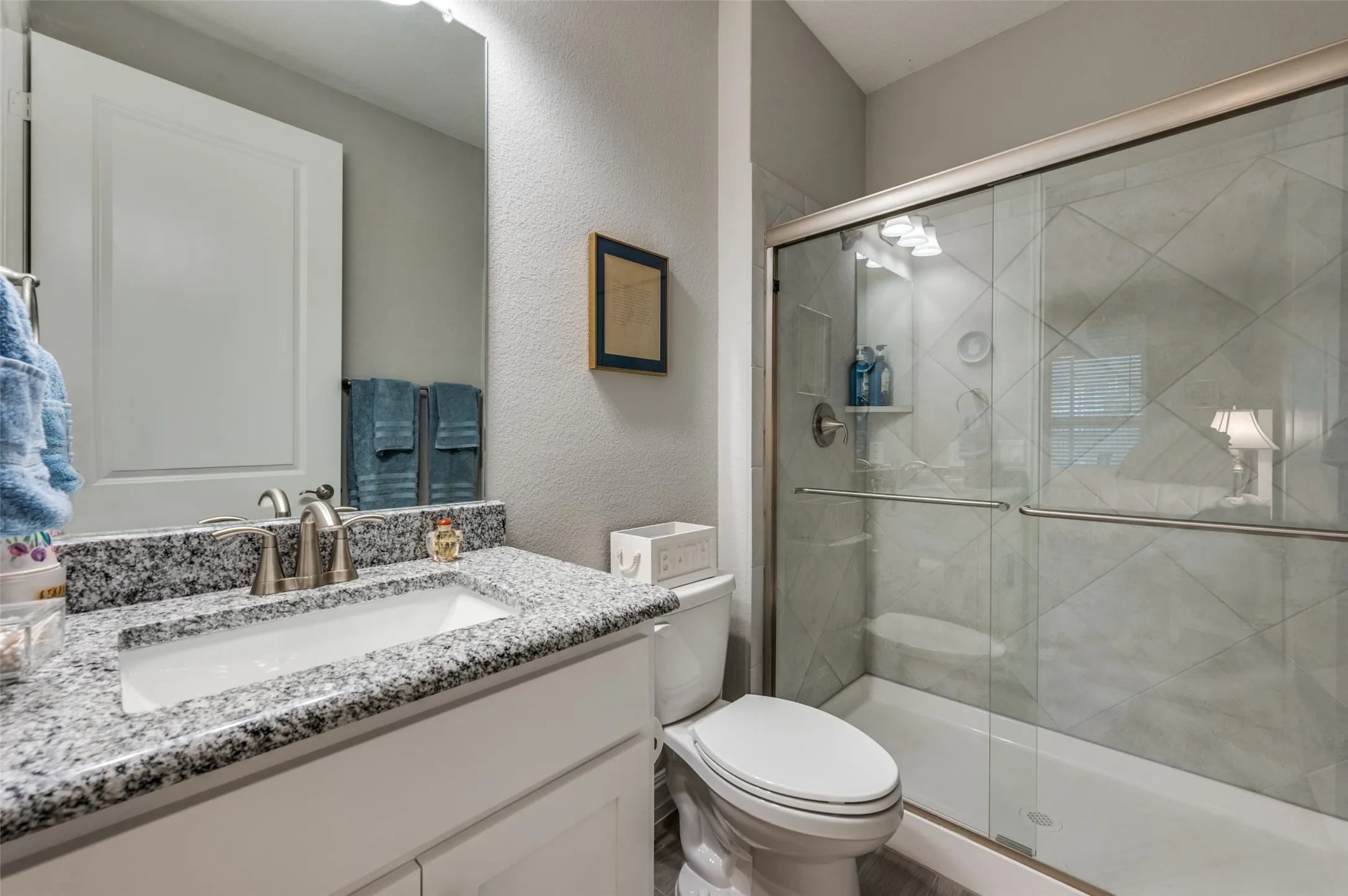 Bathroom featuring a vanity with a white rectangular sink and speckled countertop, brushed nickel faucet, and a tiled shower with a sliding glass door