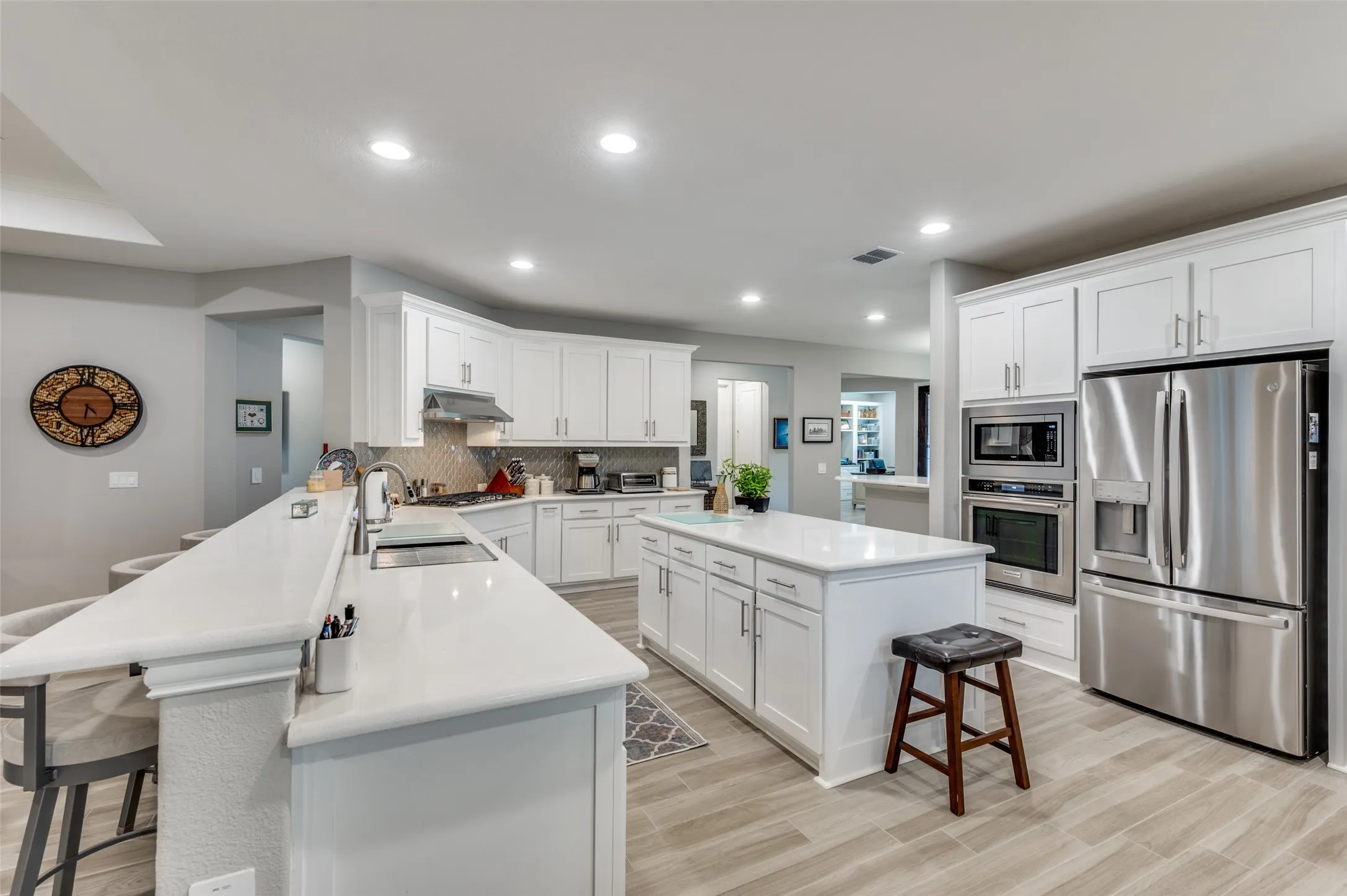 Gourmet kitchen featuring white shaker cabinetry, stainless steel appliances, a central island, and light-toned wood-look flooring