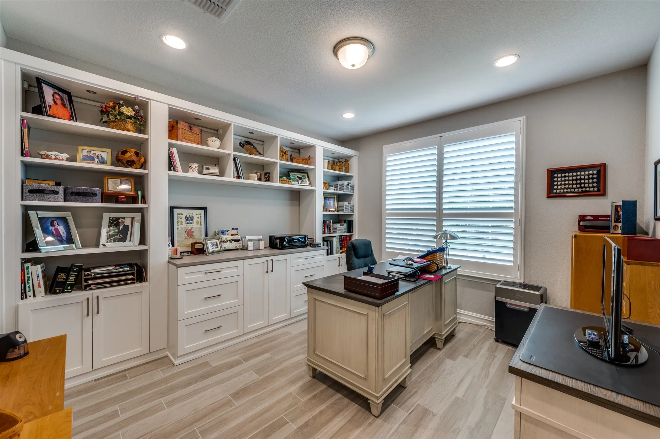 Built-in custom cabinetry with open shelving and closed storage, recessed lighting, wood-finish flooring, and window with plantation shutters
