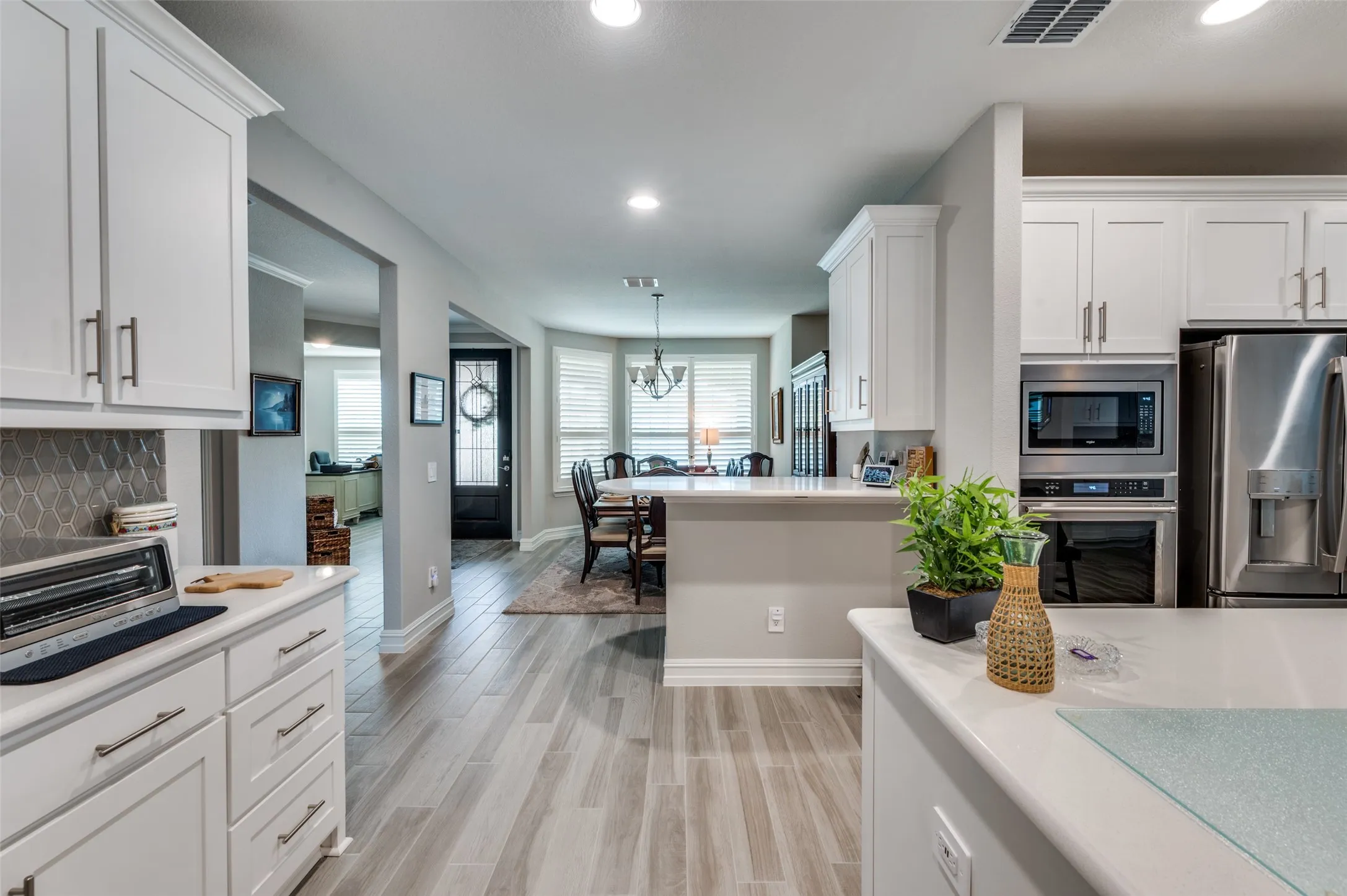 Spacious kitchen featuring light wood-finish flooring, white cabinetry with silver hardware, an integrated stainless steel microwave and oven, a side-by-side stainless steel refrigerator, and light countertops