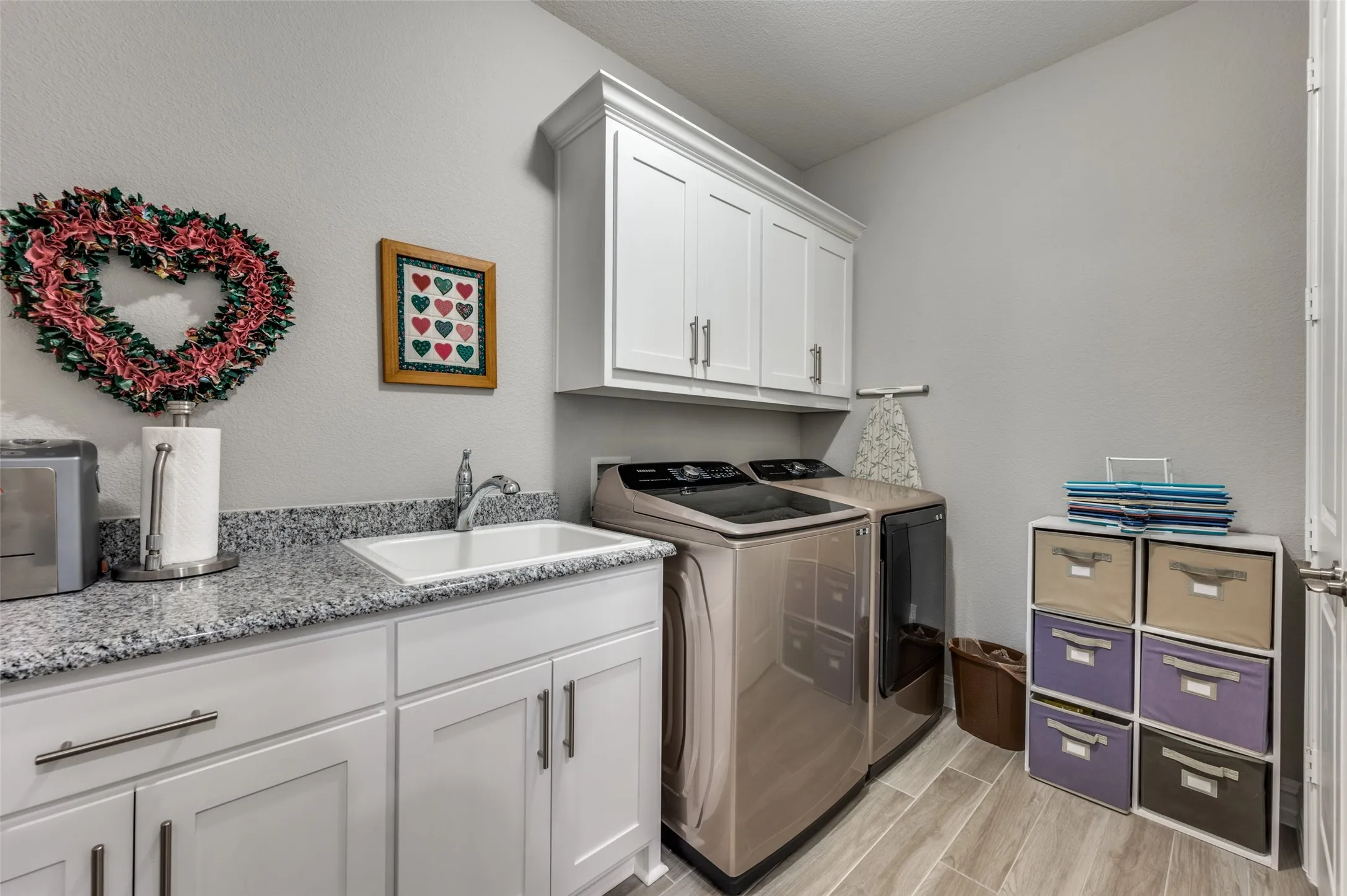 Utility room featuring light wood-finish plank flooring, white cabinetry with brushed nickel hardware, and granite-style countertops