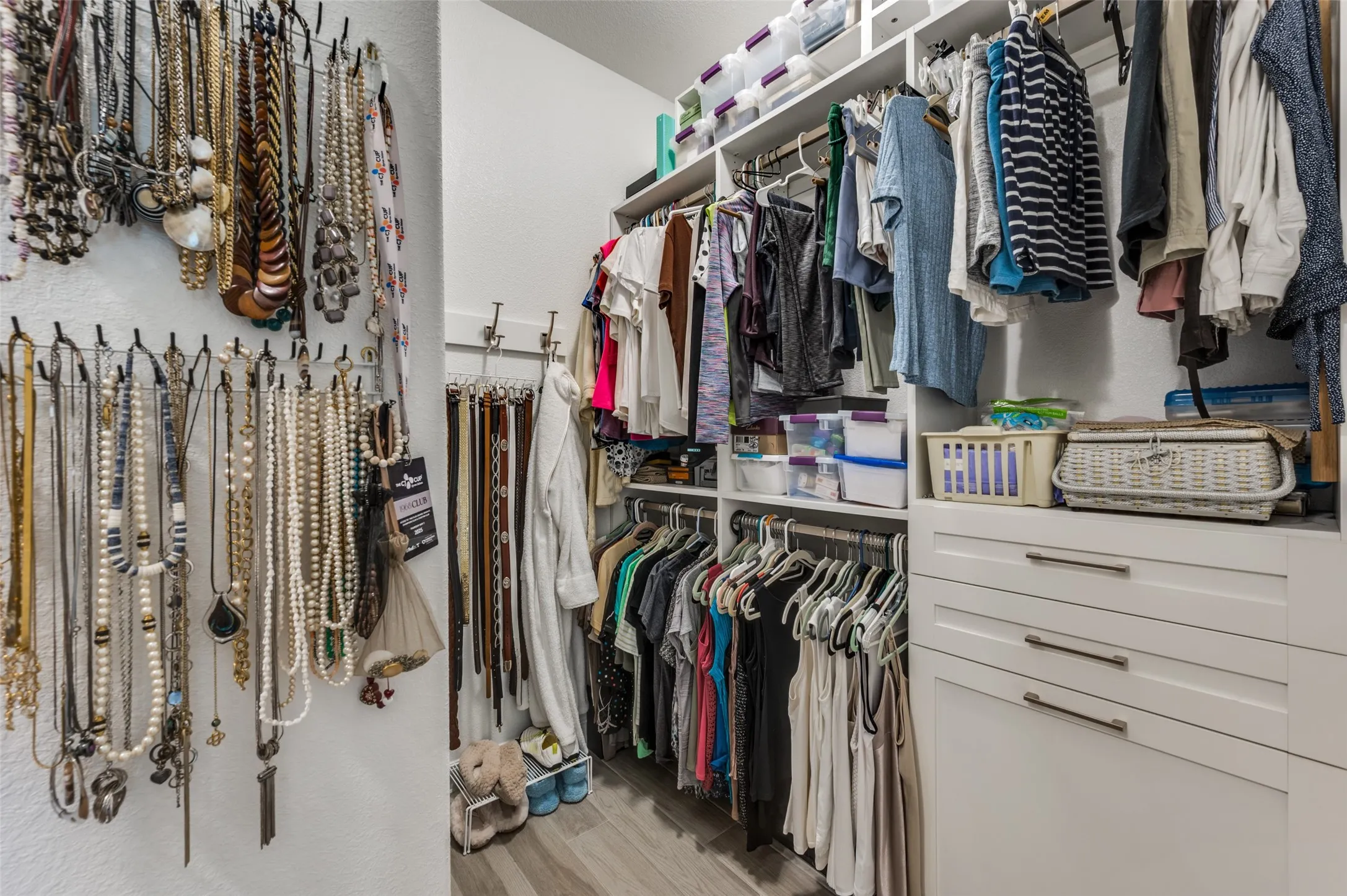Custom closet system featuring white cabinetry, multiple hanging rods, integrated shelving, and drawer storage with contemporary pulls