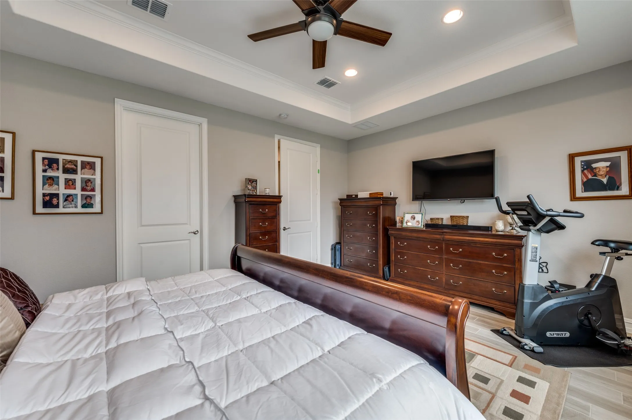 Recessed lighting illuminates a tray ceiling with a dark wood-finish ceiling fan