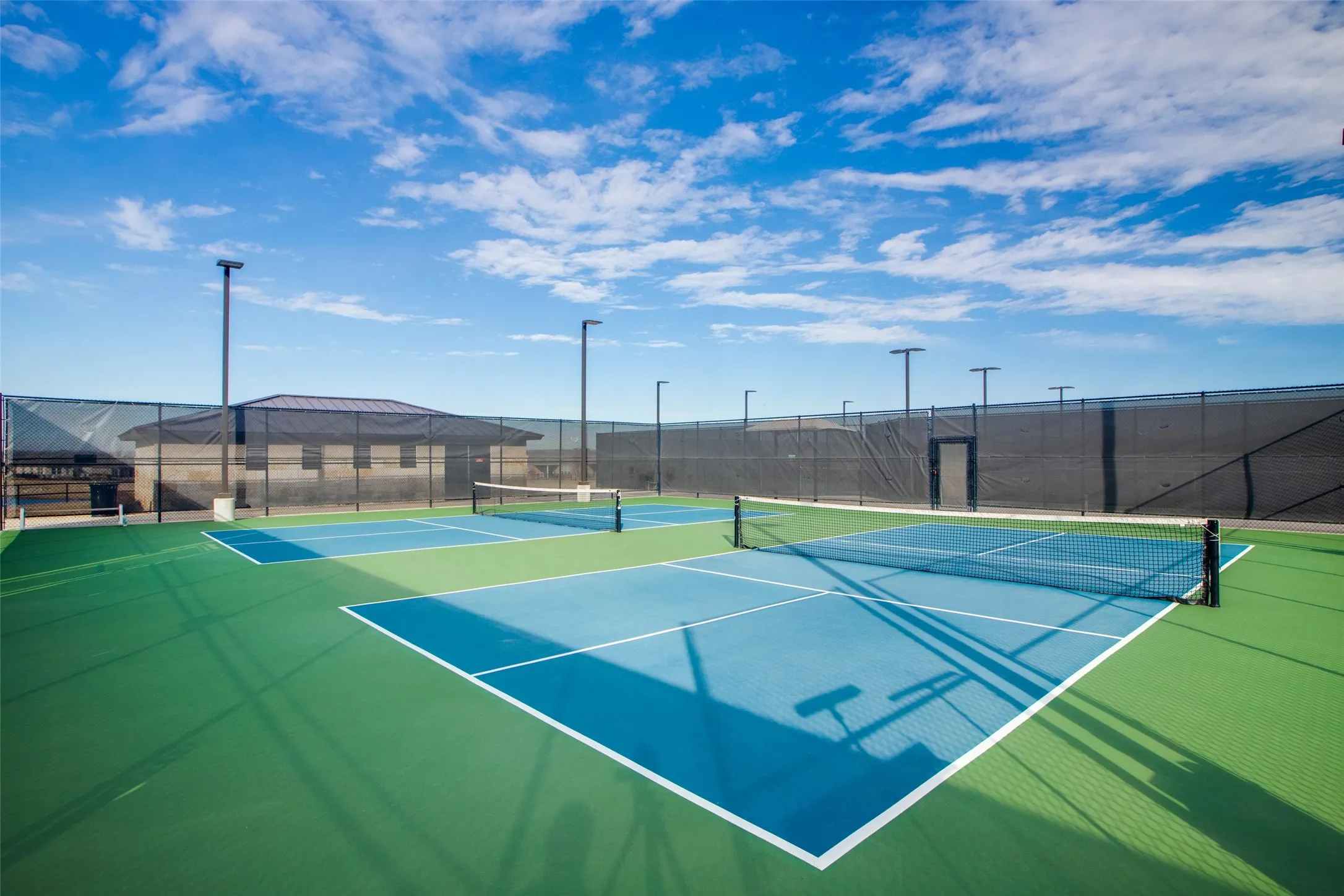 Multiple outdoor courts with blue and green surfacing, featuring perimeter fencing and overhead lighting