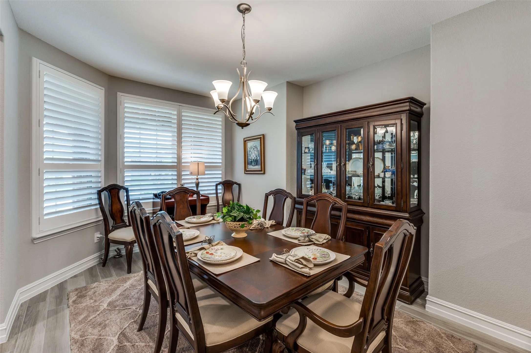 Dining area featuring wood-finish flooring, white plantation shutters, a multi-light chandelier, and a built-in display cabinet