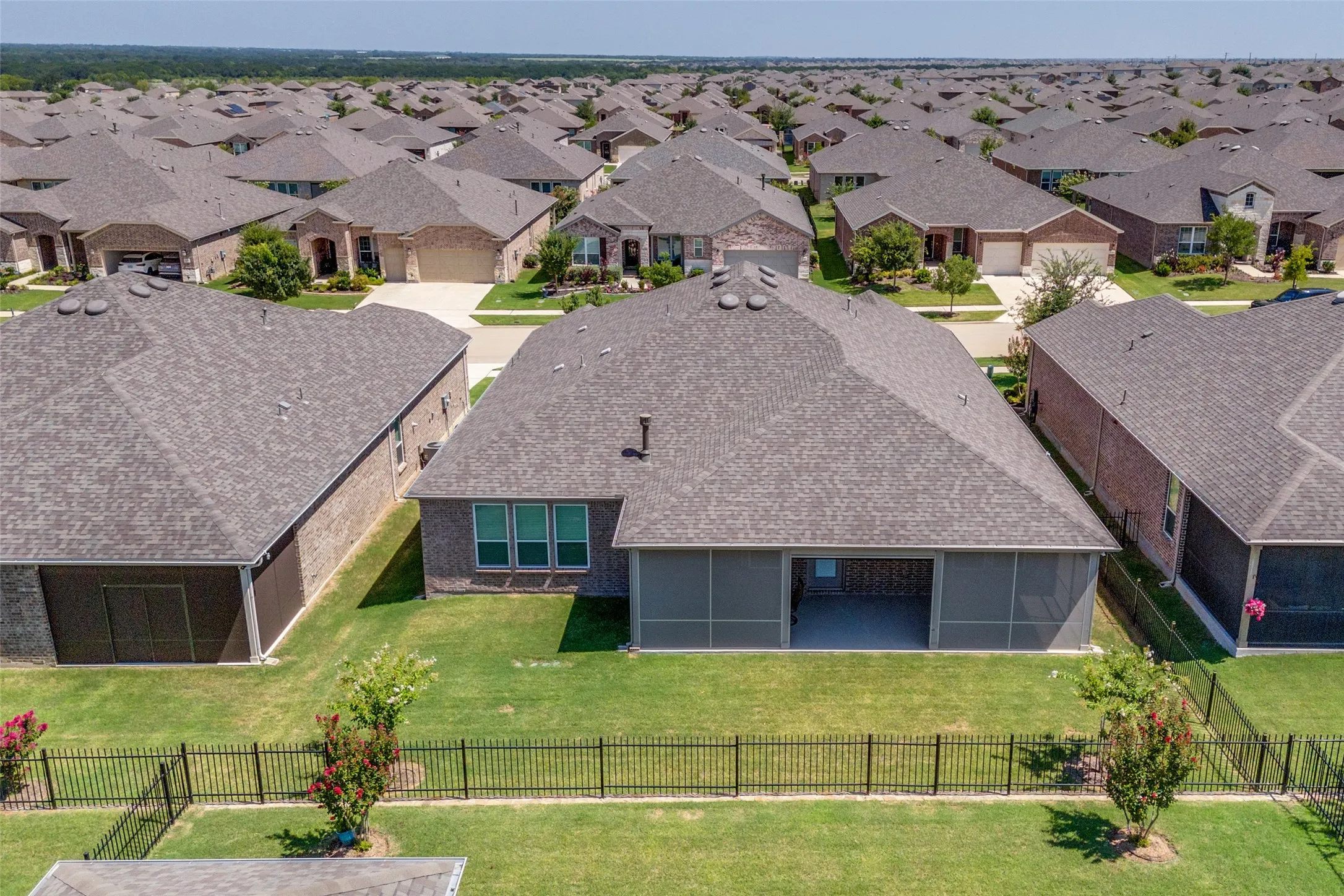 Rear exterior featuring a screened-in patio, three large rear windows, a dark shingle roof, and a black wrought iron fence enclosing a manicured lawn