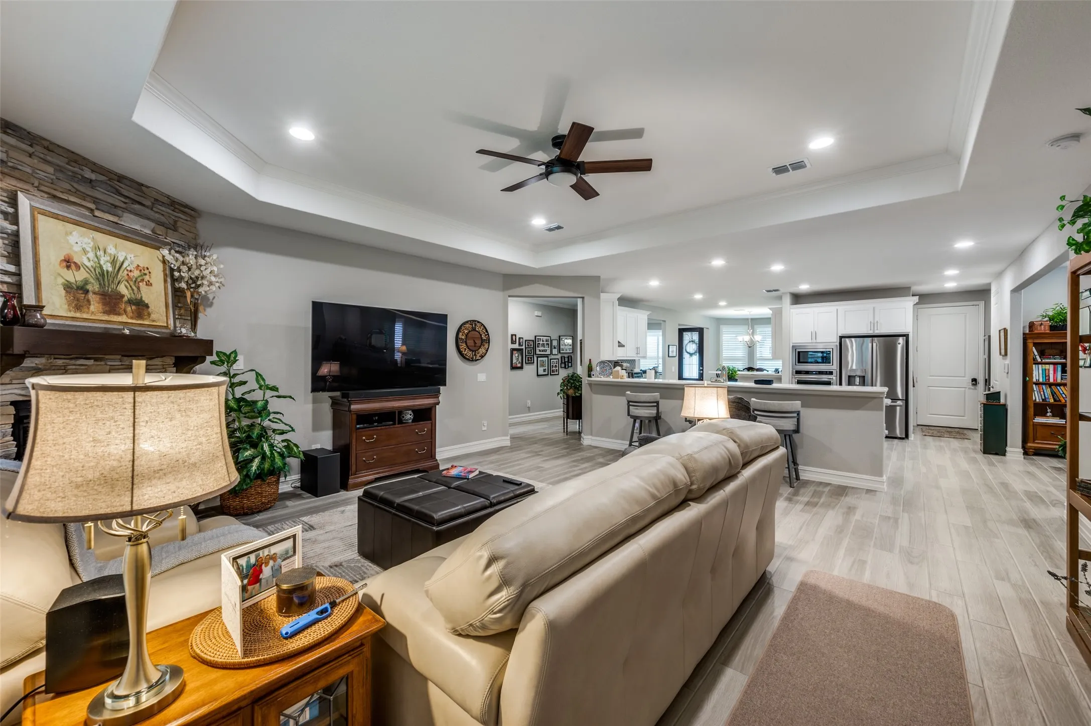 Spacious living area featuring a stacked stone fireplace with a wood mantle, wood-finish flooring, recessed lighting, and a tray ceiling