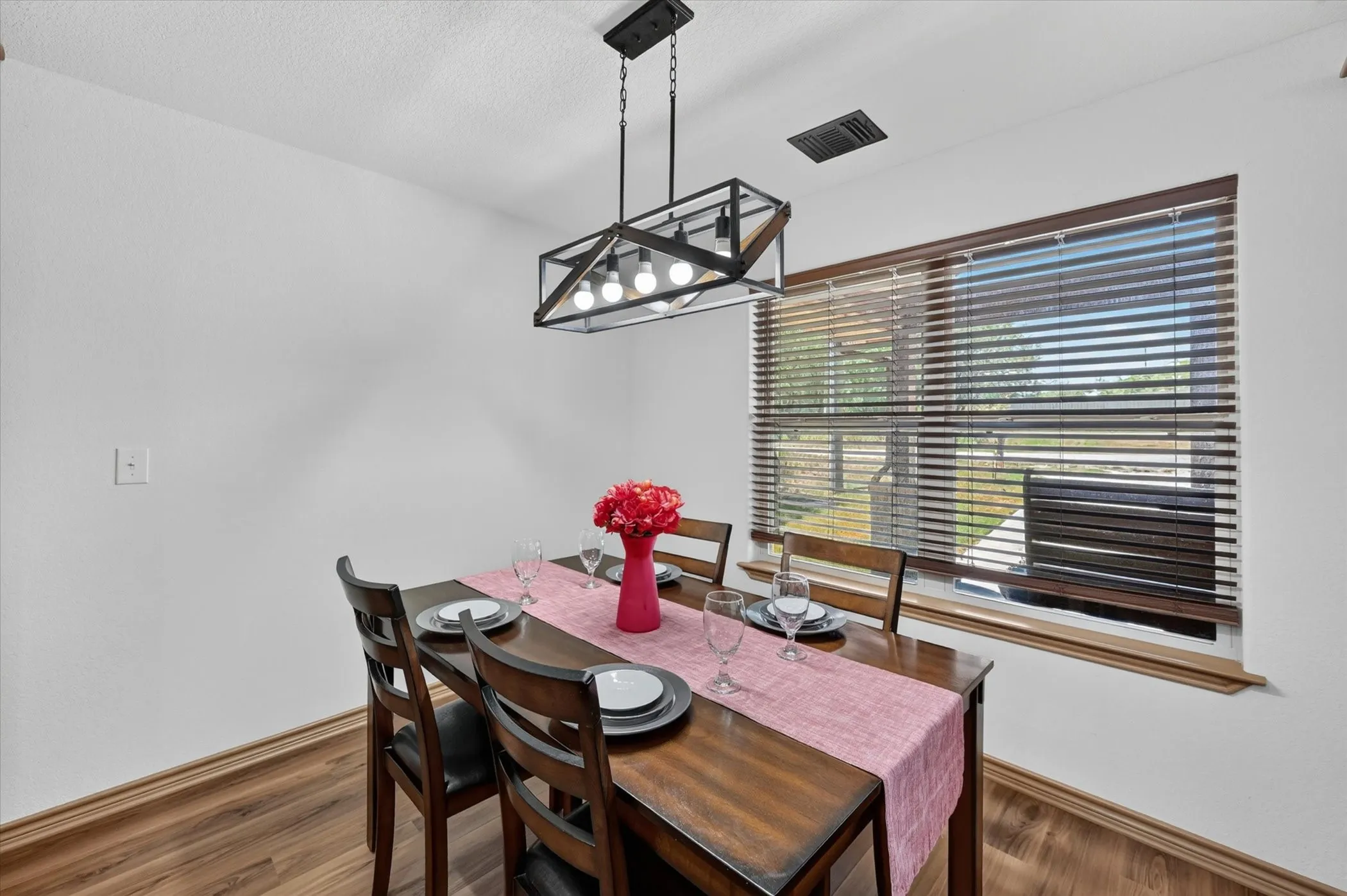 Dining area featuring wood-finish flooring, white walls, and a large window with horizontal blinds