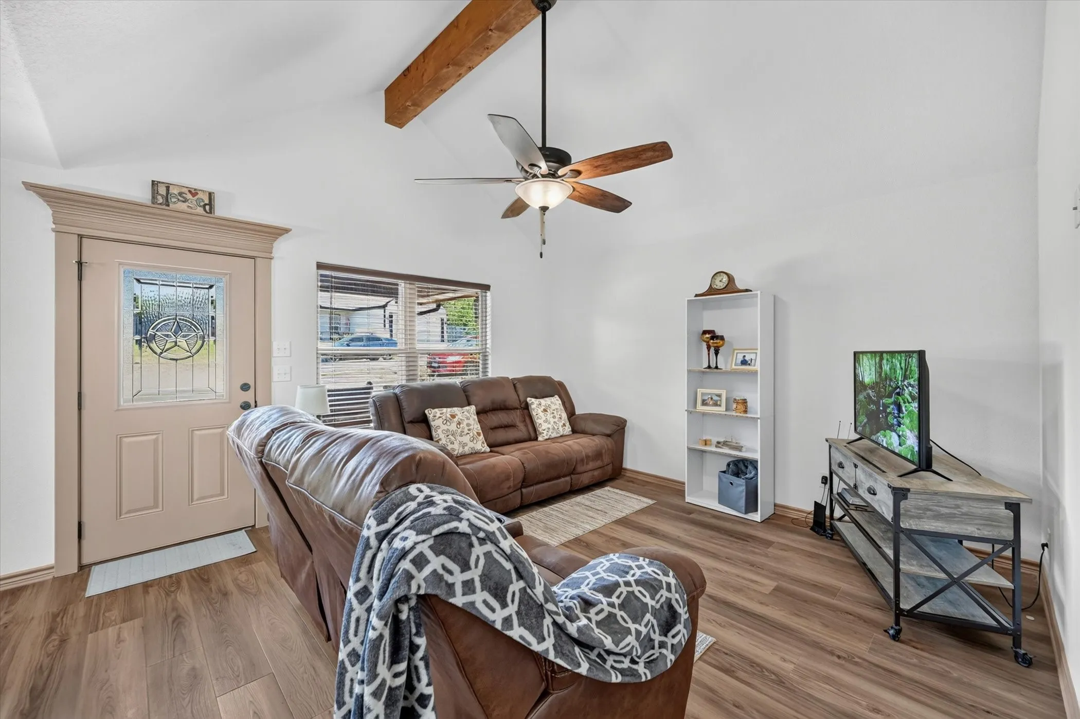 Vaulted ceiling with exposed wood beam, ceiling fan, wood-finish flooring, and a decorative front entry door with a star-patterned glass insert