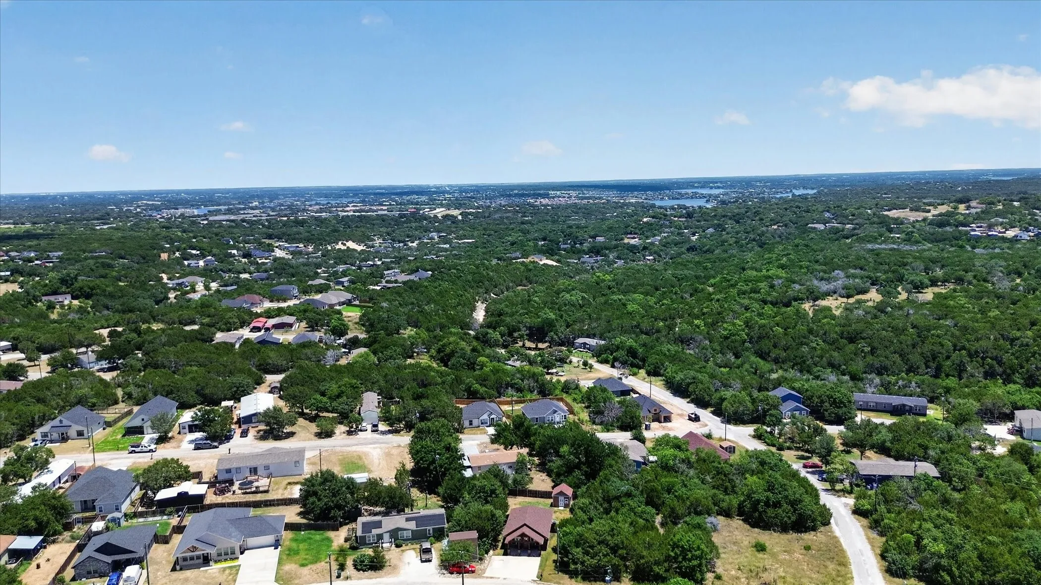 Expansive aerial showcasing a residential neighborhood with abundant mature trees and a distant body of water
