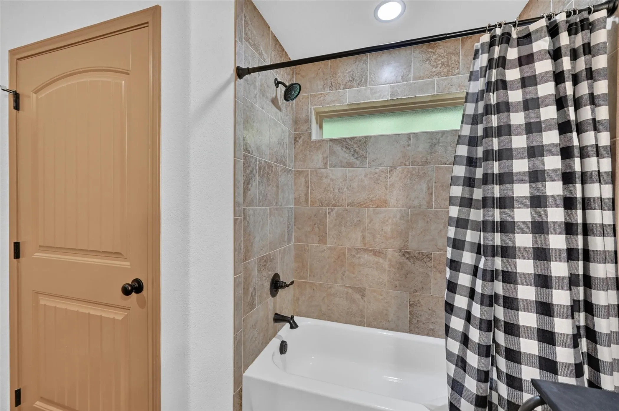 Tub and shower combination featuring floor-to-ceiling tile surround, a built-in window, and recessed lighting