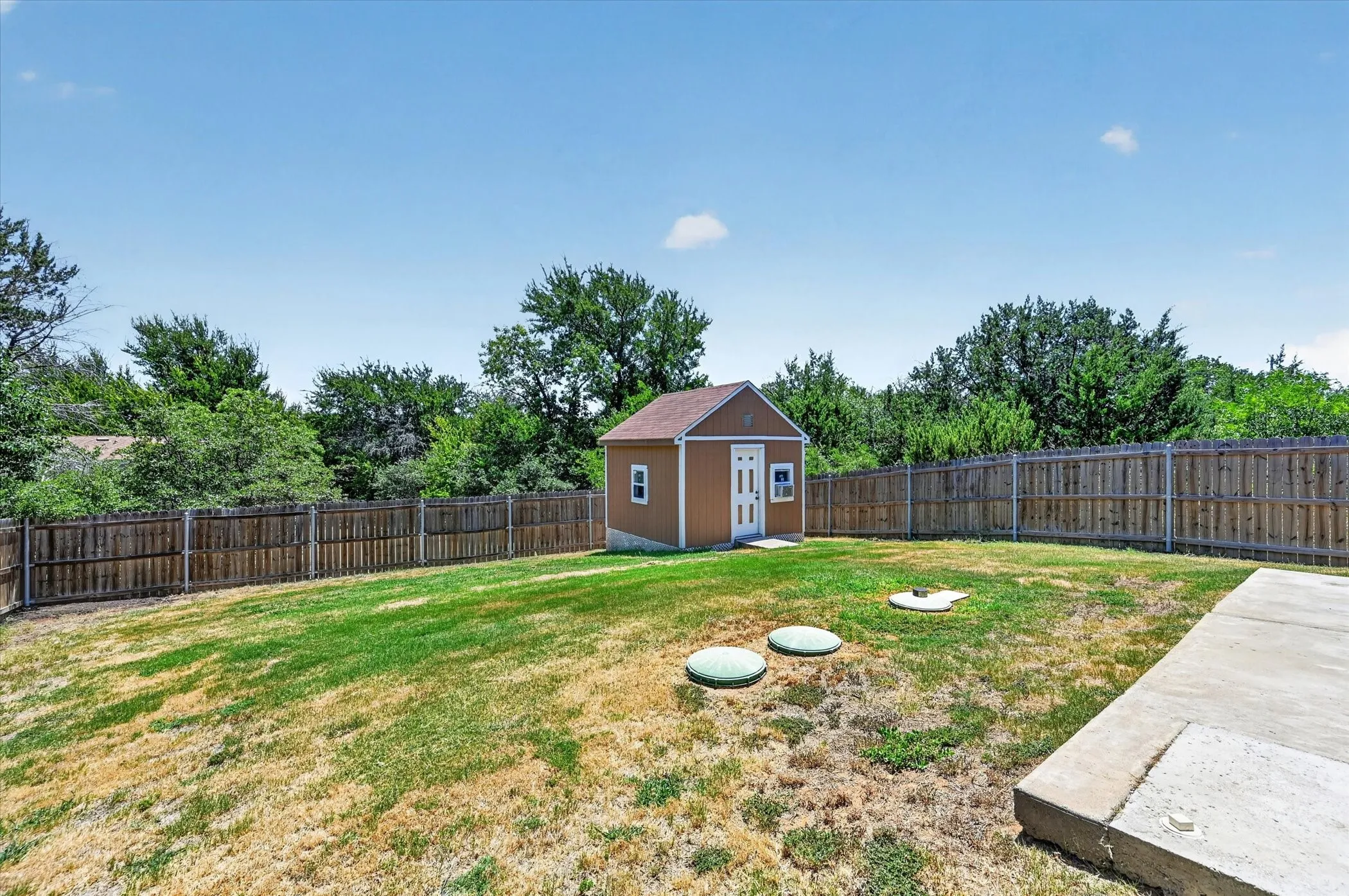 Expansive backyard featuring a storage shed with electric with white trim, full wood privacy fencing, and a concrete patio section