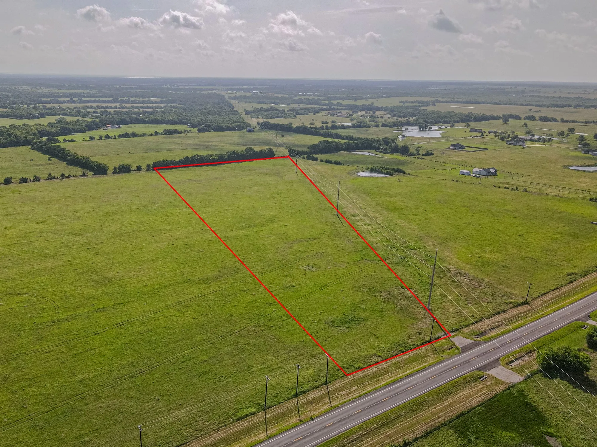 Expansive green acreage featuring a clear boundary line, direct road frontage, and a rural setting