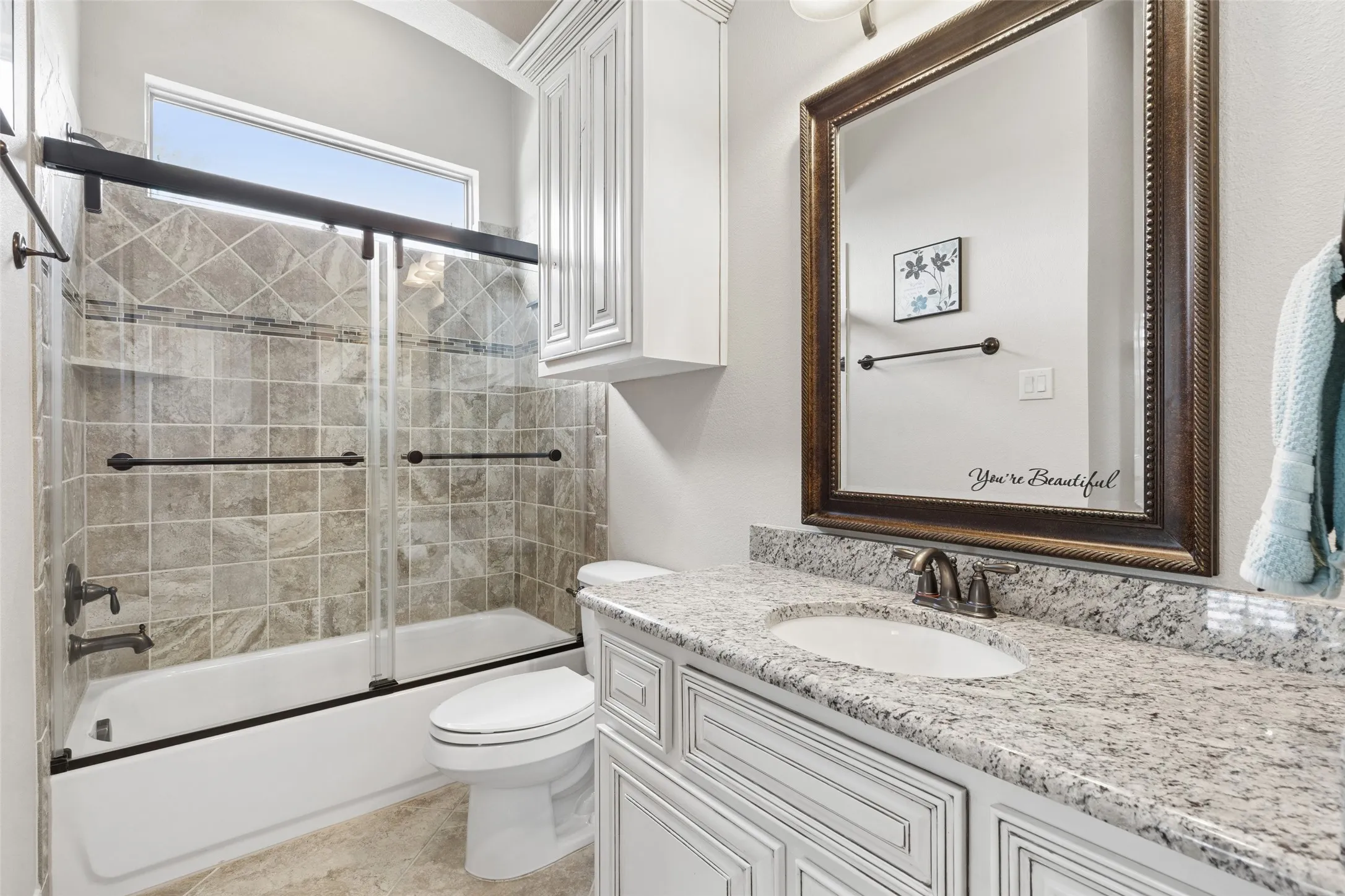Bathroom featuring a granite-topped vanity with an undermount sink, white cabinetry with decorative molding, and a framed mirror