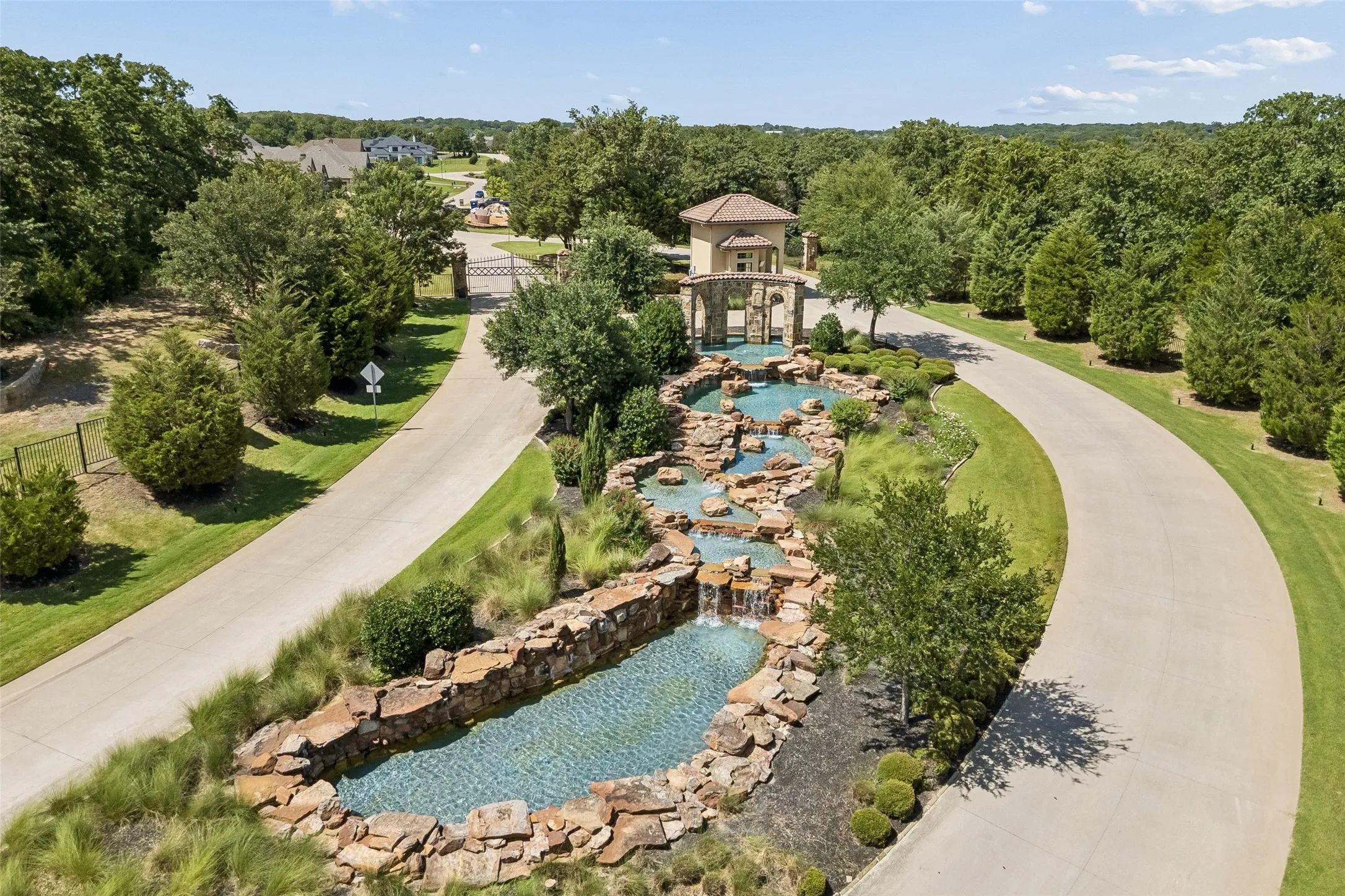Gated community entrance featuring a multi-tiered water feature with stone accents and lush landscaping