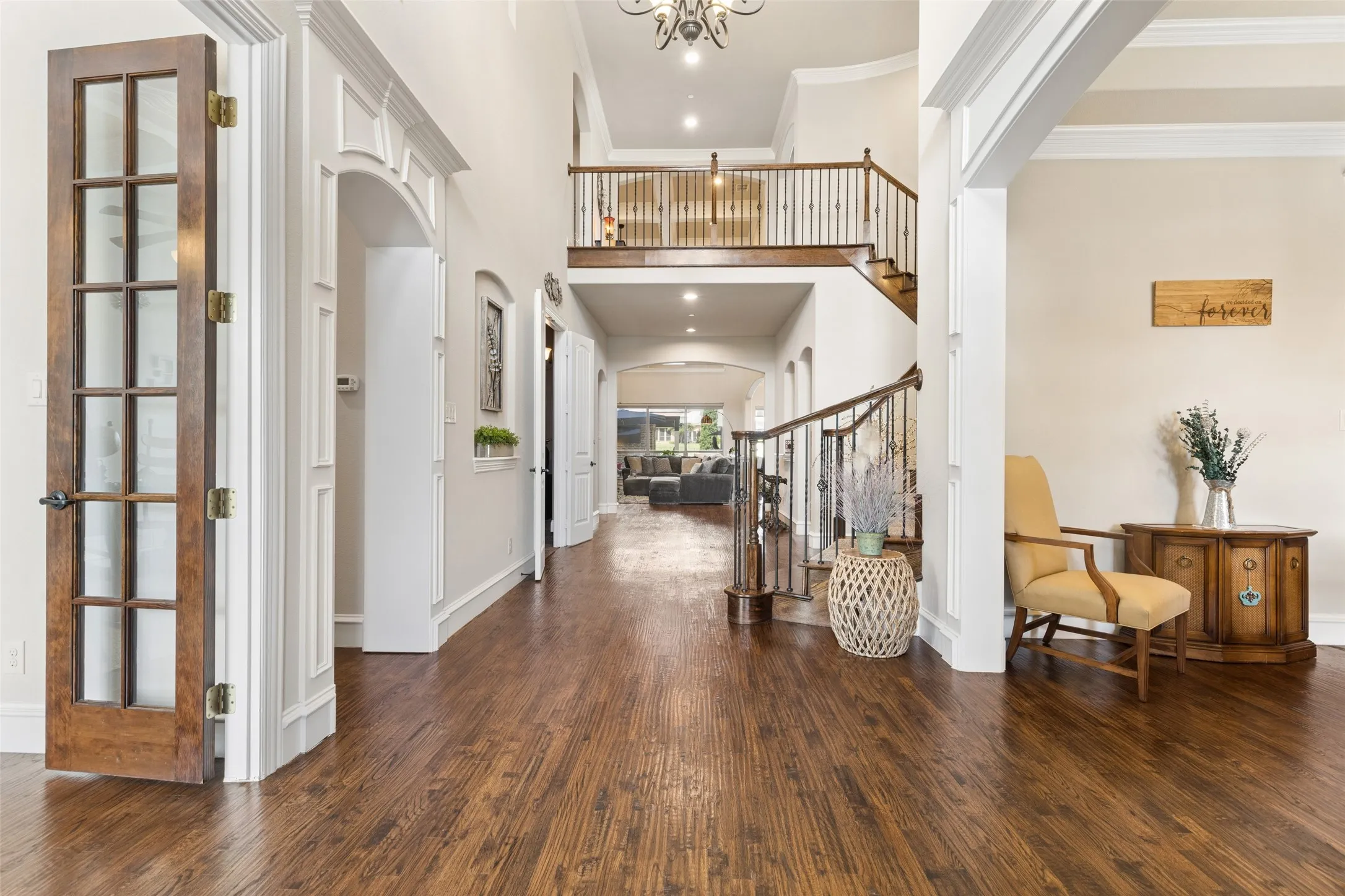Grand foyer featuring a two-story ceiling, wood-finish flooring, a prominent staircase with dark wood handrails and wrought iron balusters, arched doorways, and white paneled walls