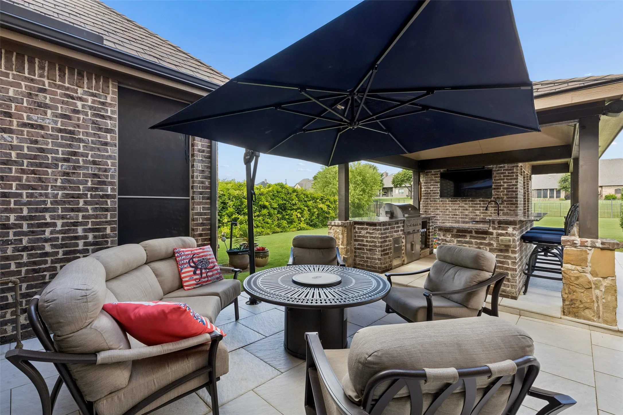Outdoor living area featuring a built-in brick kitchen with a grill, sink, and bar seating