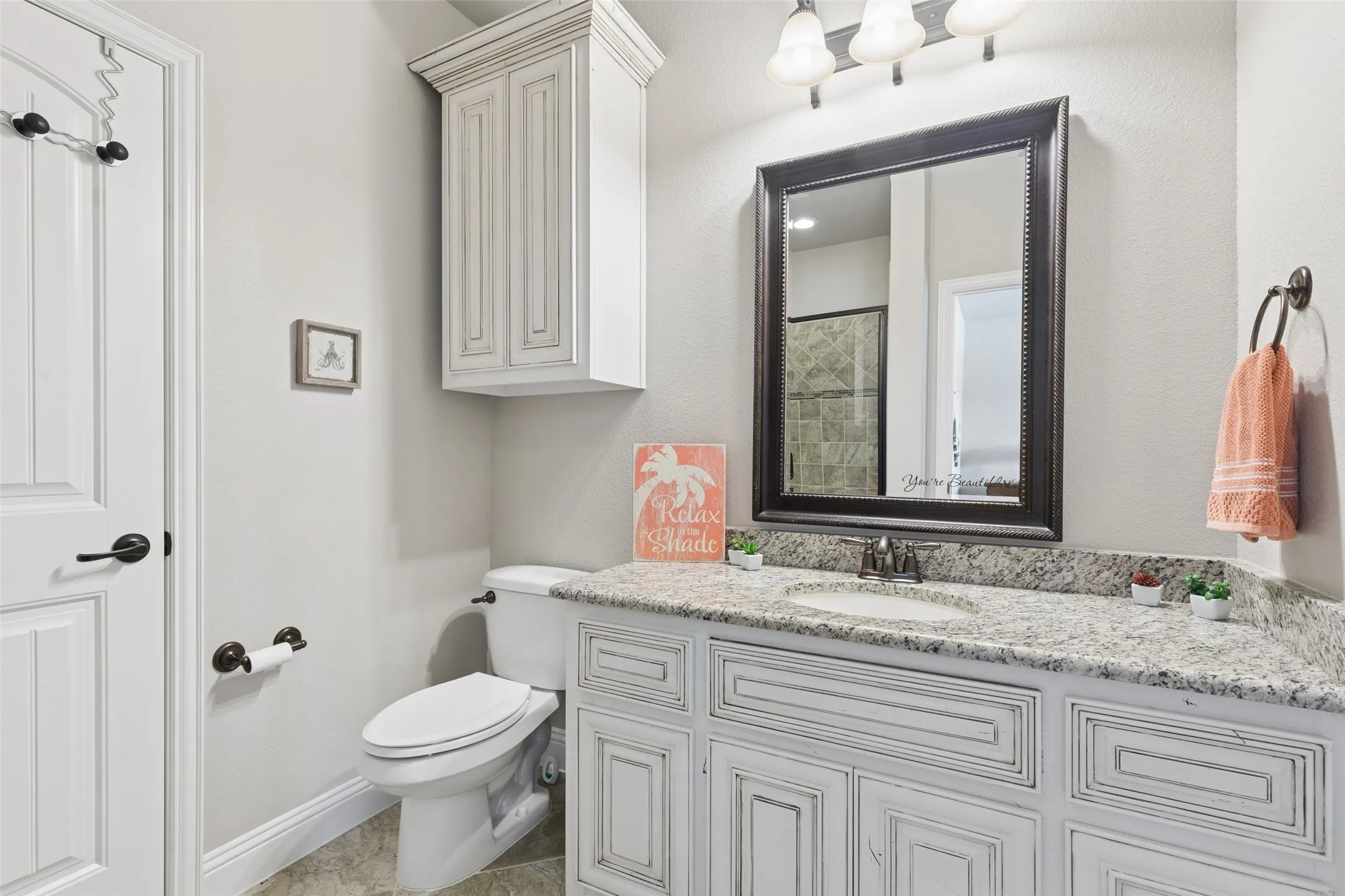 Bathroom featuring a white vanity with textured cabinetry, a speckled countertop, an undermount sink, and a dark-framed mirror