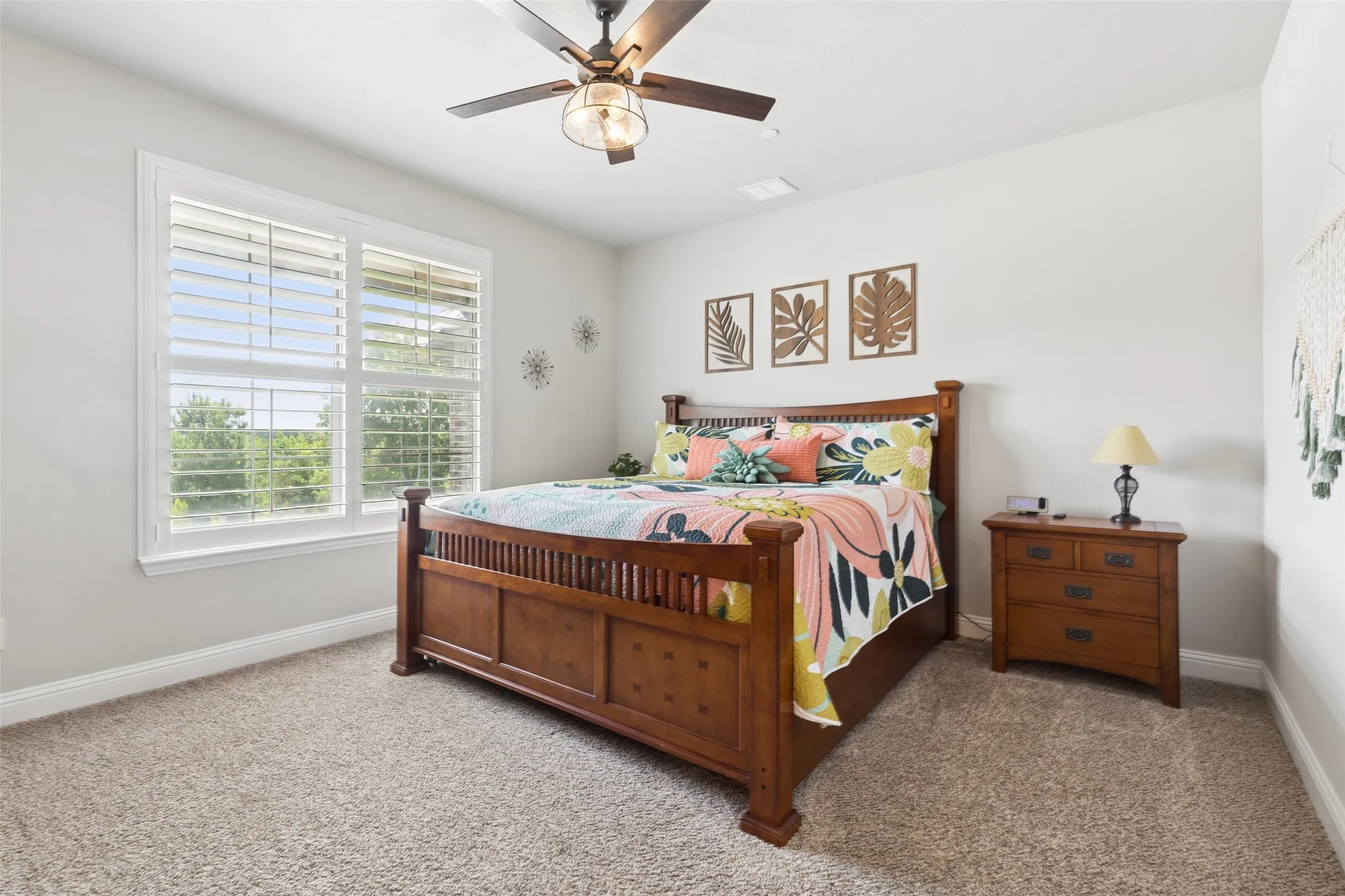 Bright room featuring a ceiling fan with integrated lighting, a large window with white plantation shutters, and light-colored carpet flooring