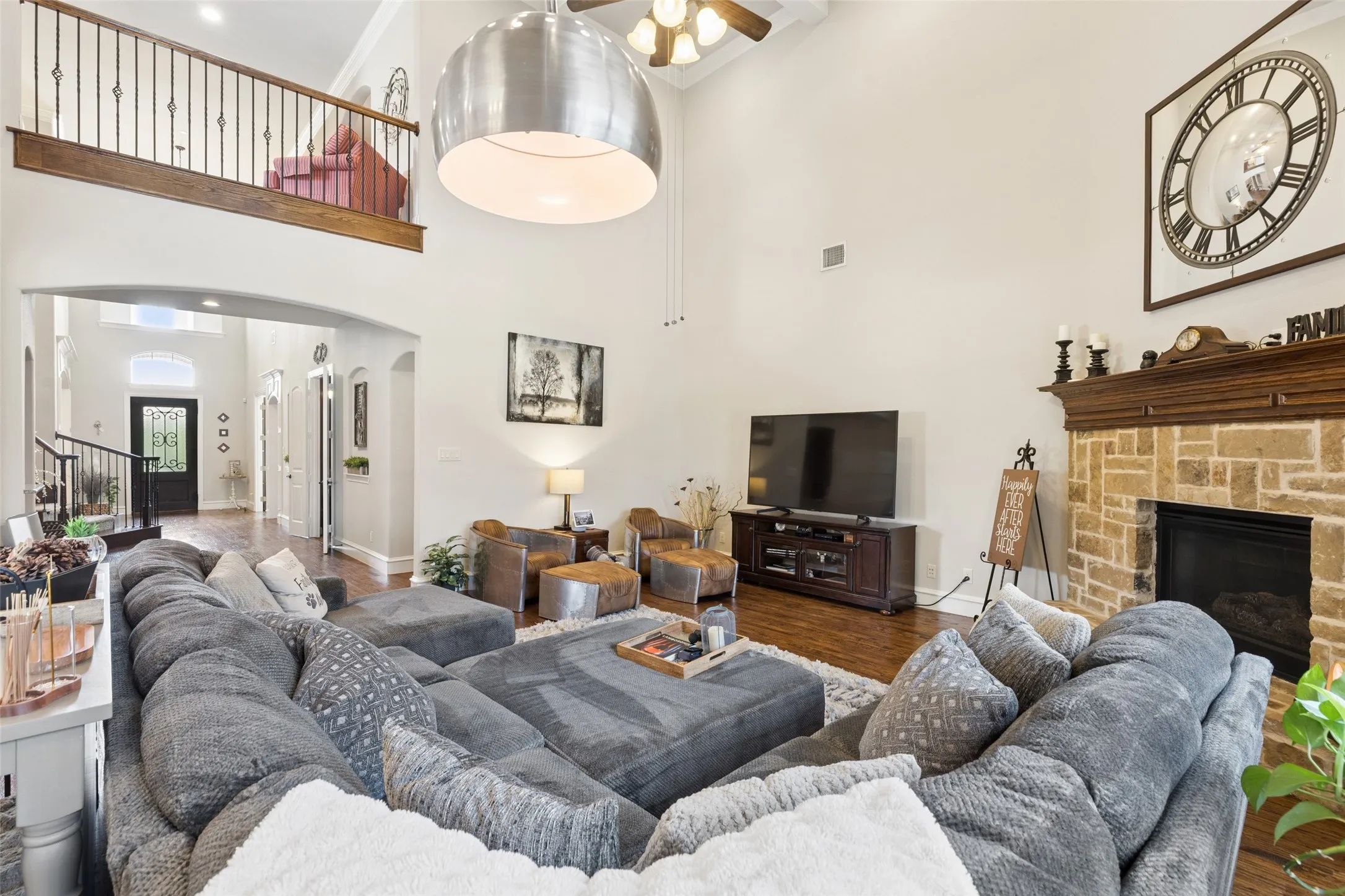 Vaulted living area featuring a stone-clad fireplace with a wood mantle, wood-finish flooring, and a second-story balcony with wrought iron balusters