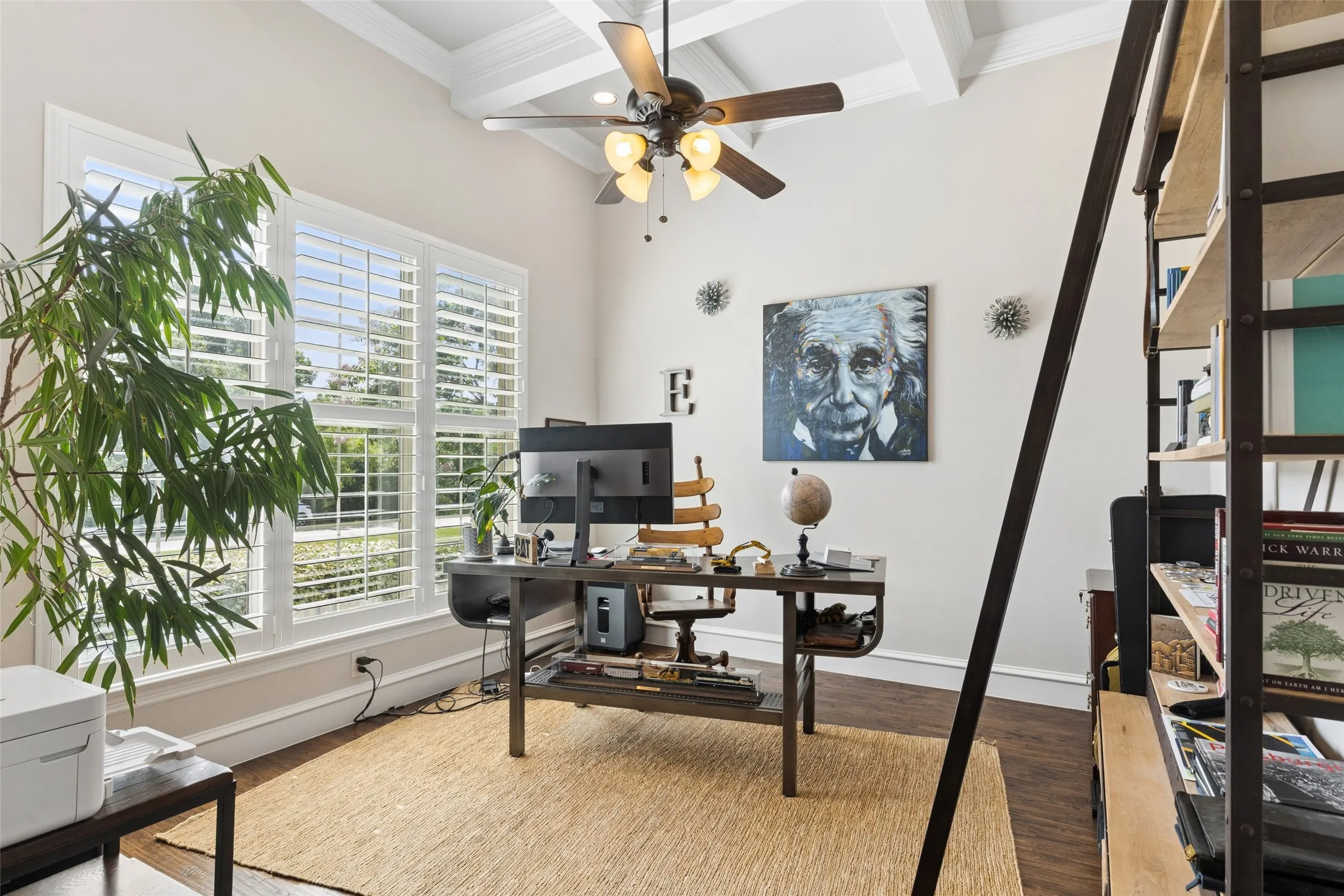 Room featuring a coffered ceiling, a ceiling fan, and multiple windows with plantation shutters