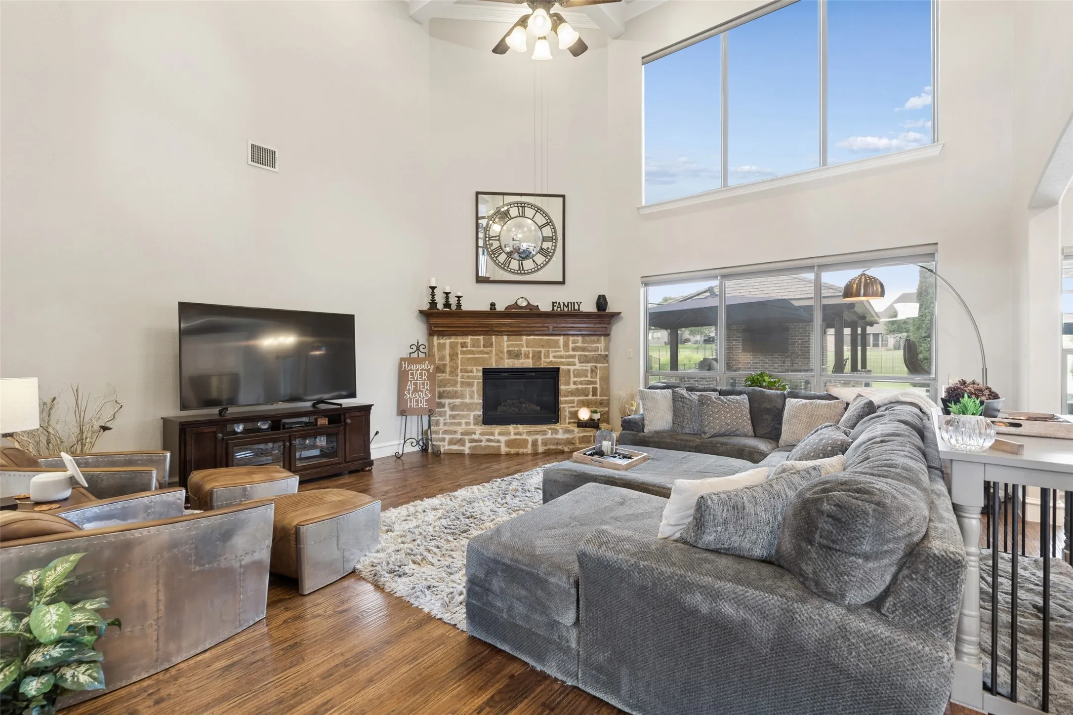 Living space featuring vaulted ceilings, a stacked stone fireplace with wood mantel, large windows, wood-finish flooring, and a ceiling fan