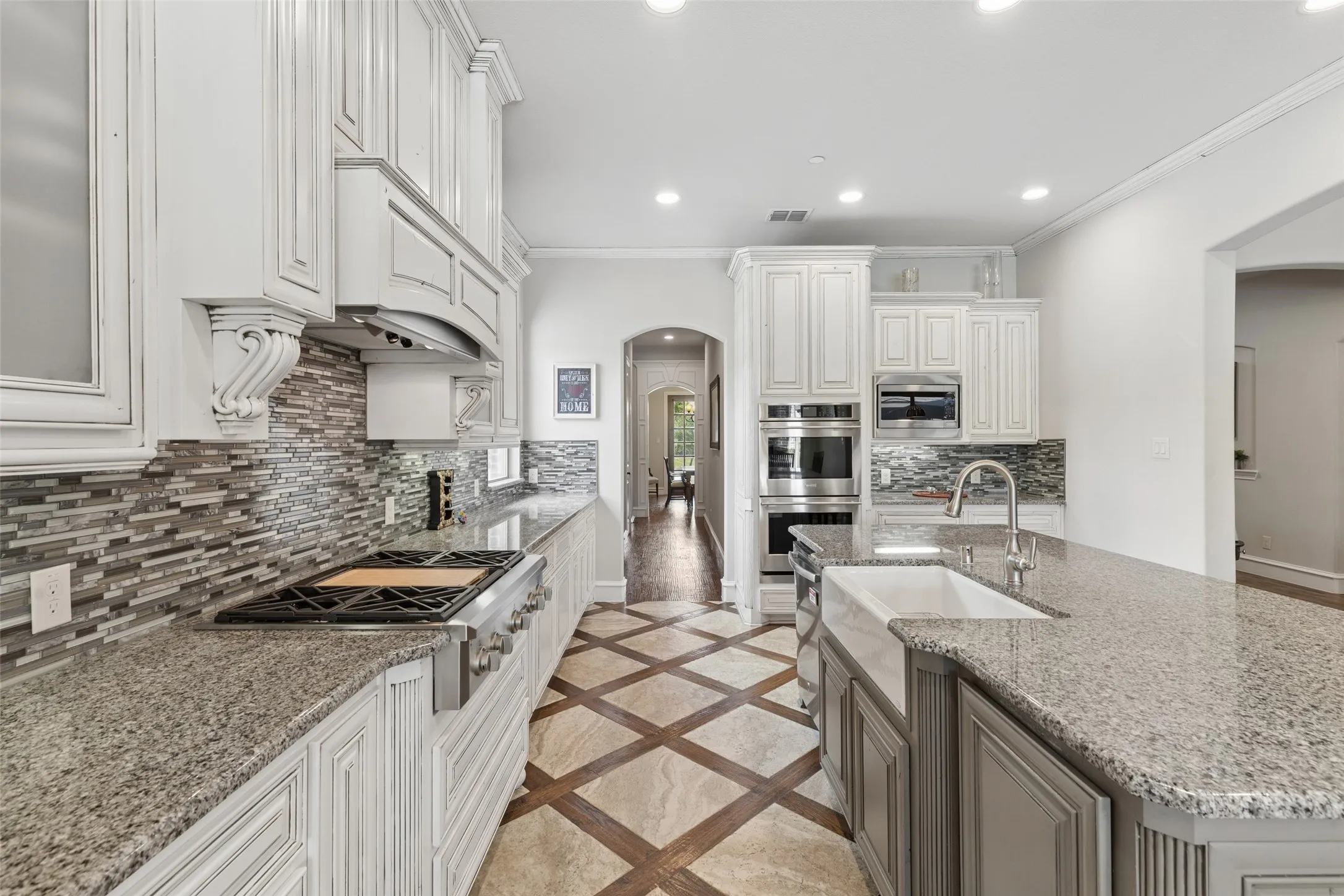 Gourmet kitchen featuring a farmhouse sink, stainless steel appliances, granite countertops, custom cabinetry, and patterned tile flooring